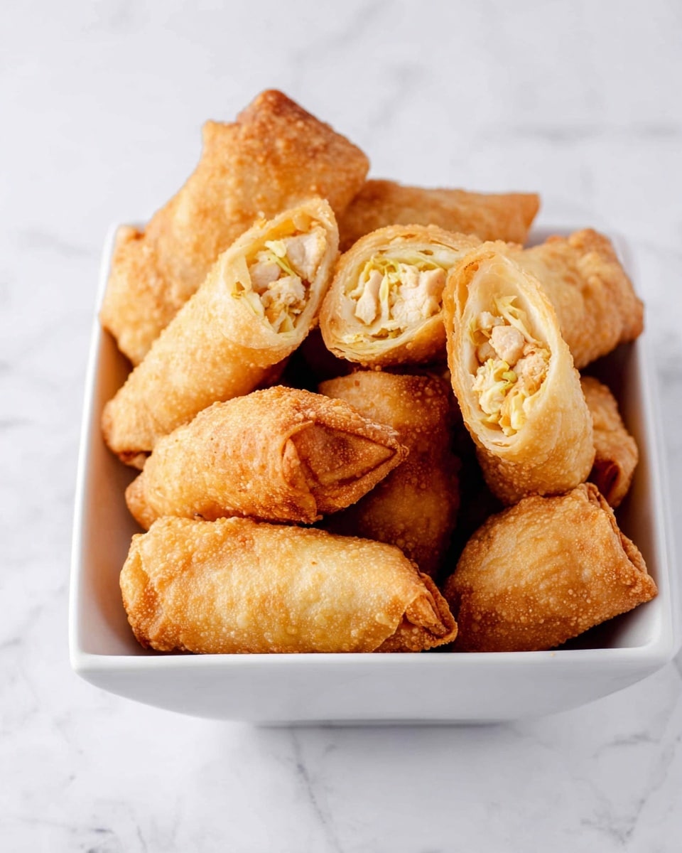 A white rectangular bowl filled with golden brown fried spring rolls with a bubbly and crispy texture. Some spring rolls are whole, tightly wrapped with a slightly uneven surface, while a few are cut in half revealing layers of finely shredded pale yellow cabbage and small pieces of light-colored chicken inside. The bowl is placed on a white marbled surface, creating a clean and bright background. photo taken with an iphone --ar 4:5 --v 7