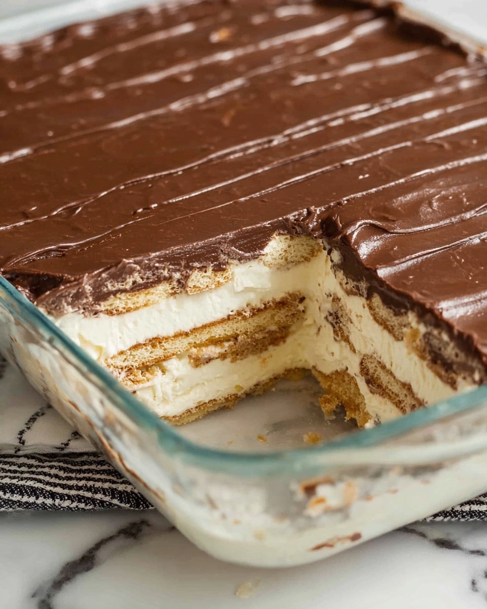 A glass rectangular dish shows a layered dessert with three main layers visible. The bottom layer is light tan, crumbly, and looks like a cookie base. Above it, there are two alternating layers of creamy white filling and crumbly cookie layers with a mix of beige and light brown tones. The top layer is a smooth, thick, glossy chocolate spread with slight ridges running vertically. A section is cut out from the corner, revealing the inside layers clearly. The dish is set on a white marbled surface with a black and white pattern partially visible beneath it. Photo taken with an iphone --ar 4:5 --v 7
