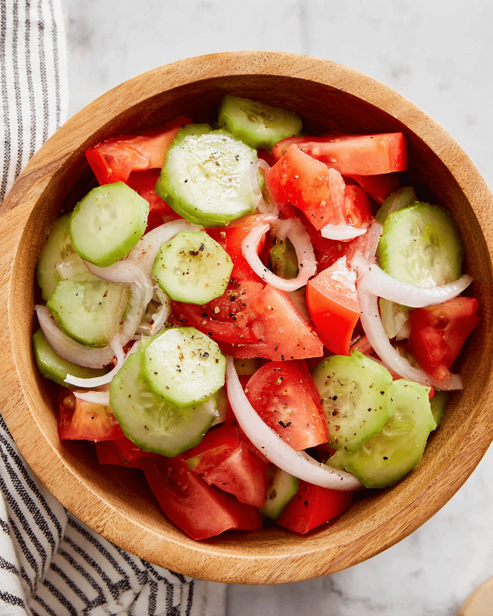 A round wooden bowl filled with a fresh salad made of three visible layers: at the bottom are light green cucumber slices with watery texture, scattered over them are bright red, juicy tomato chunks, and on top, thin white onion rings with a slight shine. The vegetables look fresh and mixed with small dark specks of seasoning. The bowl sits on a white marbled surface with a striped cloth partially visible at the edge. photo taken with an iphone --ar 4:5 --v 7