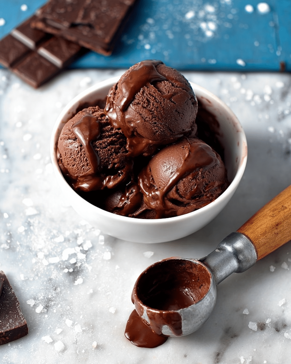 A close-up view of a white bowl filled with four scoops of rich, dark chocolate ice cream, with some glossy melted chocolate dripping down the sides, showing a creamy and smooth texture. Next to the bowl lies a silver ice cream scoop with a wooden handle, coated with melted chocolate inside the scoop part. The bowl and scoop are placed on a white marbled surface with a few scattered white granules around. In the background, there are several pieces of dark chocolate squares set loosely on the surface. Photo taken with an iphone --ar 4:5 --v 7