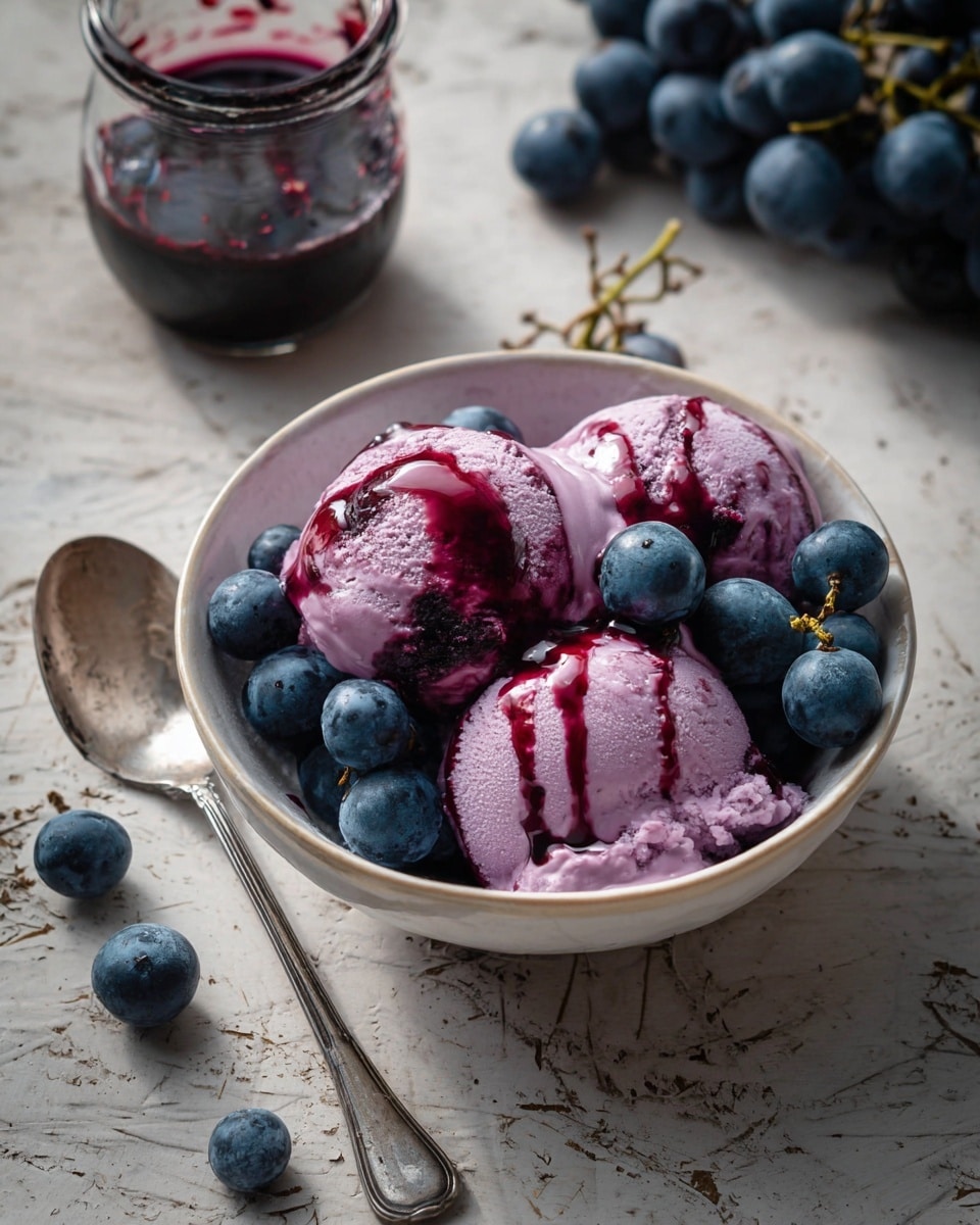 A white bowl filled with three scoops of pale purple ice cream topped with dark purple grape syrup in wavy lines, garnished with a cluster of fresh dark blue grapes resting on top and around the ice cream; a silver spoon is placed inside the bowl, all set on a white marbled textured surface with loose dark grapes around the bowl. photo taken with an iphone --ar 4:5 --v 7
