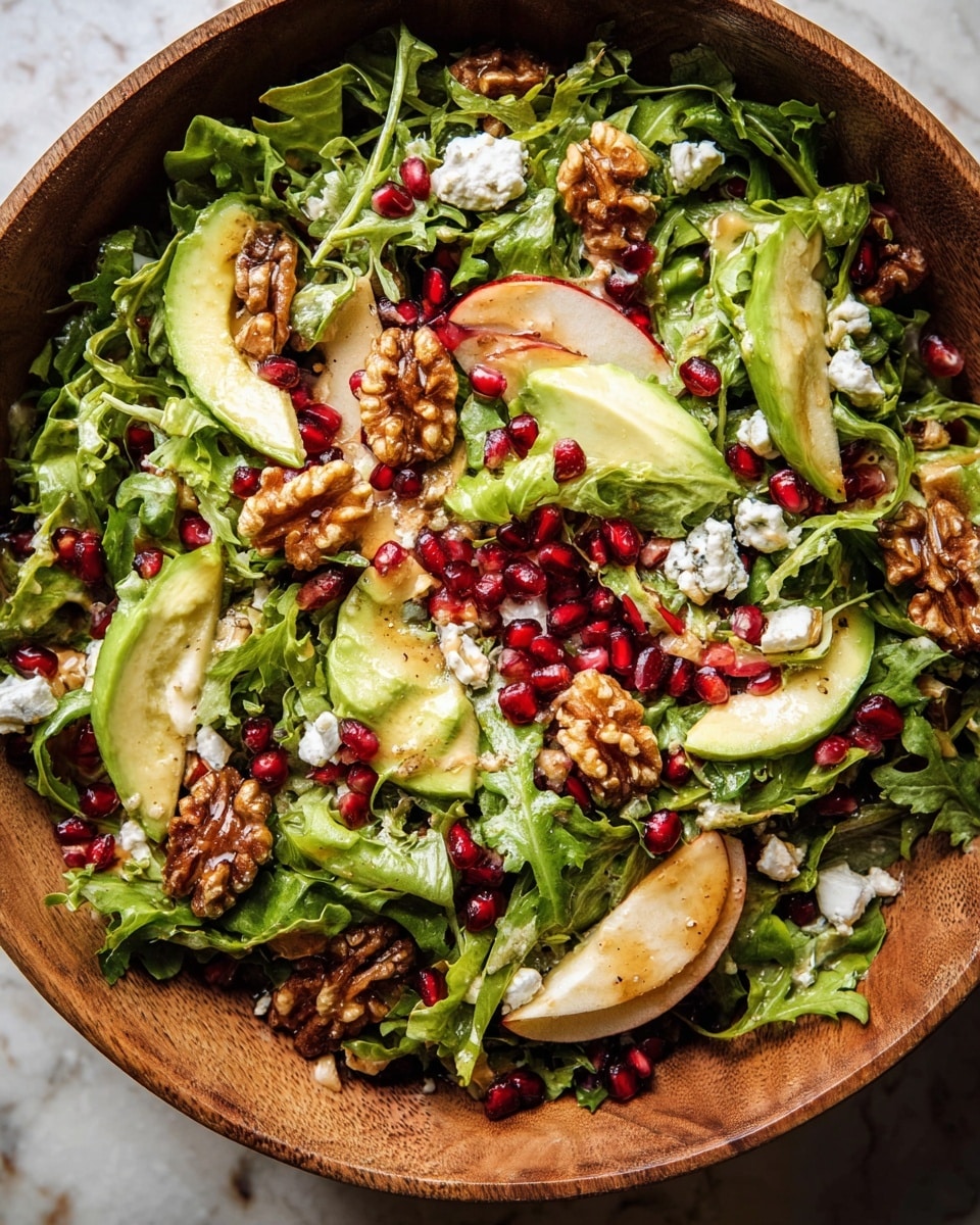 A fresh salad served in a wooden bowl features several layers: the base layer is made up of bright green curly lettuce and arugula leaves with a slightly rough texture. Scattered throughout are deep red pomegranate seeds adding small shiny bursts of color. There are thick slices of creamy light green avocado with smooth surfaces nestled among the greens. Pieces of light beige apple slices with reddish skin can be seen peeking through. Walnut halves with a textured, brownish surface are placed on top, adding a crunchy look. Small crumbles of white cheese with a crumbly texture are sprinkled over the salad. The whole dish has a light drizzle of golden dressing that adds a soft shine. The wooden bowl sits on a white marbled textured surface. photo taken with an iphone --ar 4:5 --v 7