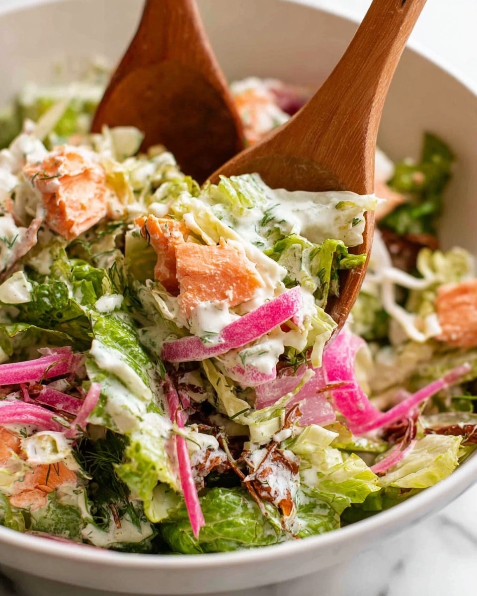 A close-up image of a fresh salad in a white bowl set on a white marbled surface, showing layers of bright green leafy lettuce, vibrant pink pickled onions, shredded white cabbage, and chunks of light orange salmon mixed with a creamy white dressing that has green herbs. Two wooden salad spoons are lightly gripping the salad from above, lifting a mix of all the ingredients. Photo taken with an iphone --ar 4:5 --v 7