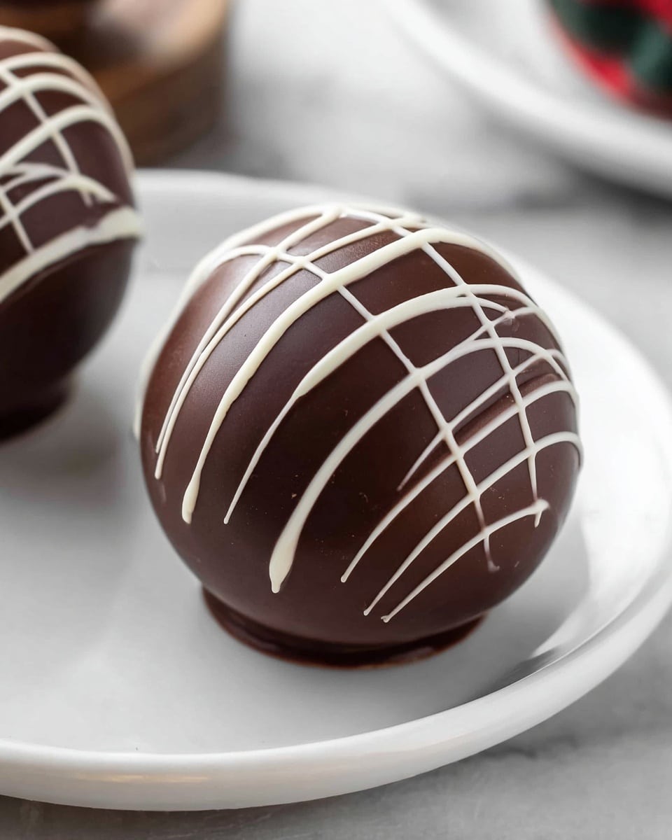 The image shows a round chocolate ball with a smooth, glossy dark brown chocolate surface, decorated with thin, irregular white chocolate lines drizzled across the top and sides. The chocolate ball rests on a simple white plate, with part of another similar chocolate ball visible. The white chocolate drizzle creates a light contrast to the dark chocolate, emphasizing the round shape and smooth texture of the dessert. The plate is placed on a white marbled surface, adding a clean and elegant look to the setup. photo taken with an iphone --ar 4:5 --v 7