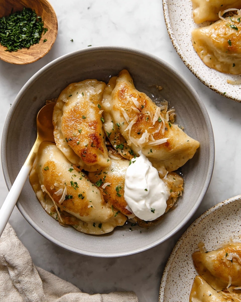 A grey bowl holds four golden brown fried dumplings sprinkled with small green herbs and thin caramelized onion pieces, with a dollop of white sour cream resting on top of one dumpling on the right side; a white and gold spoon sits inside the bowl on the left with its tip under the dumplings. To the right, there is part of a white speckled plate with more dumplings visible on a white marbled surface, with a small wood bowl containing chopped herbs placed at the upper left corner. Photo taken with an iphone --ar 4:5 --v 7