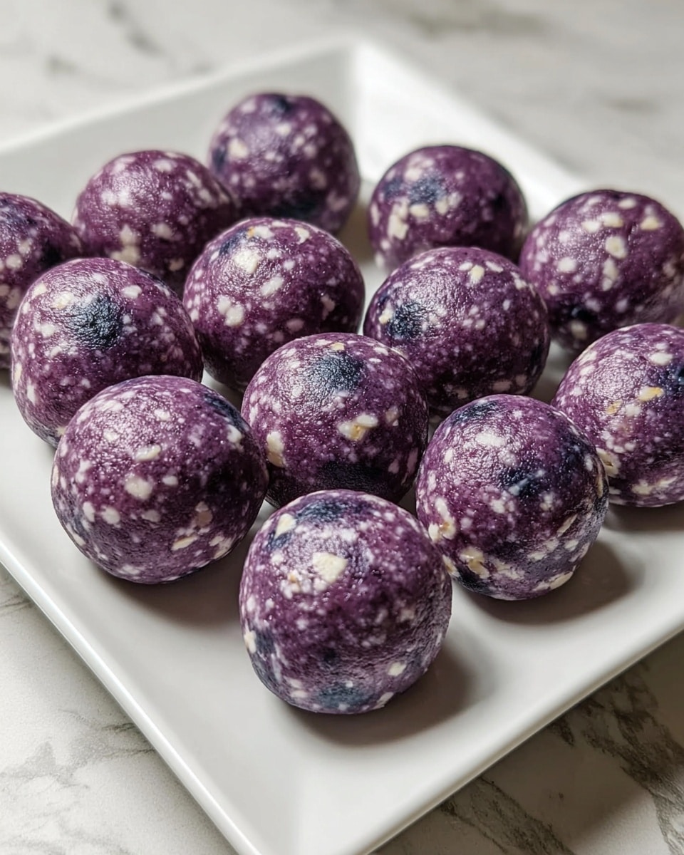 The image shows about thirteen round energy balls placed closely together on a white square plate, all on a white marbled textured surface. Each ball is purple with a mix of small white flakes and visible dark blue spots, giving them a textured look. The balls have a smooth, slightly shiny surface and are evenly sized, creating a neat and clean presentation. Photo taken with an iphone --ar 4:5 --v 7