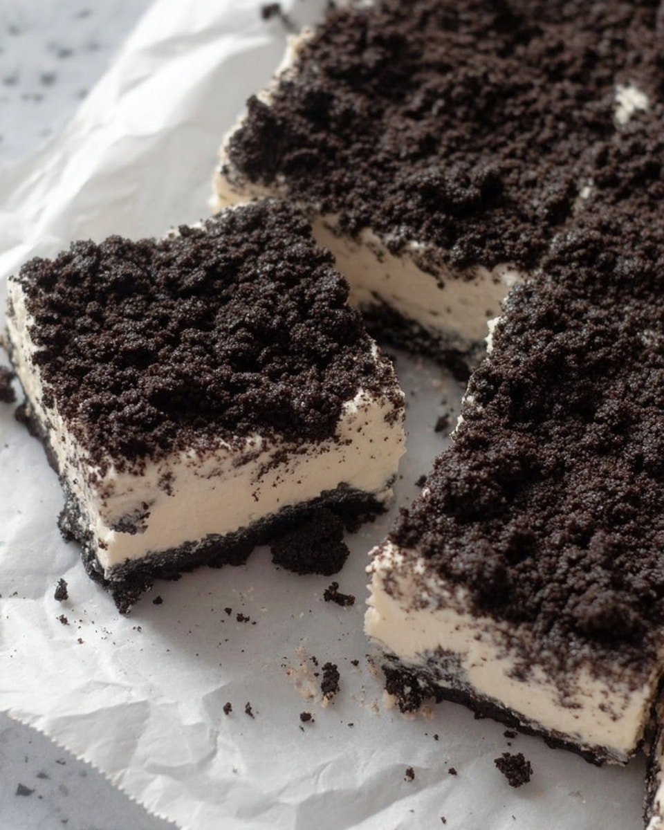 The image shows a dessert cut into square pieces placed on crumpled white parchment paper. It has two visible layers: the bottom layer is thick and creamy white with a smooth texture, and the top layer is a thick, crumbly dark brown or black cookie crumb topping scattered evenly across the surface. Some crumbs are loose around the edges, and one piece is slightly pulled away from the rest. The dessert's edges appear soft and slightly uneven. The background is a white marbled surface. photo taken with an iphone --ar 4:5 --v 7