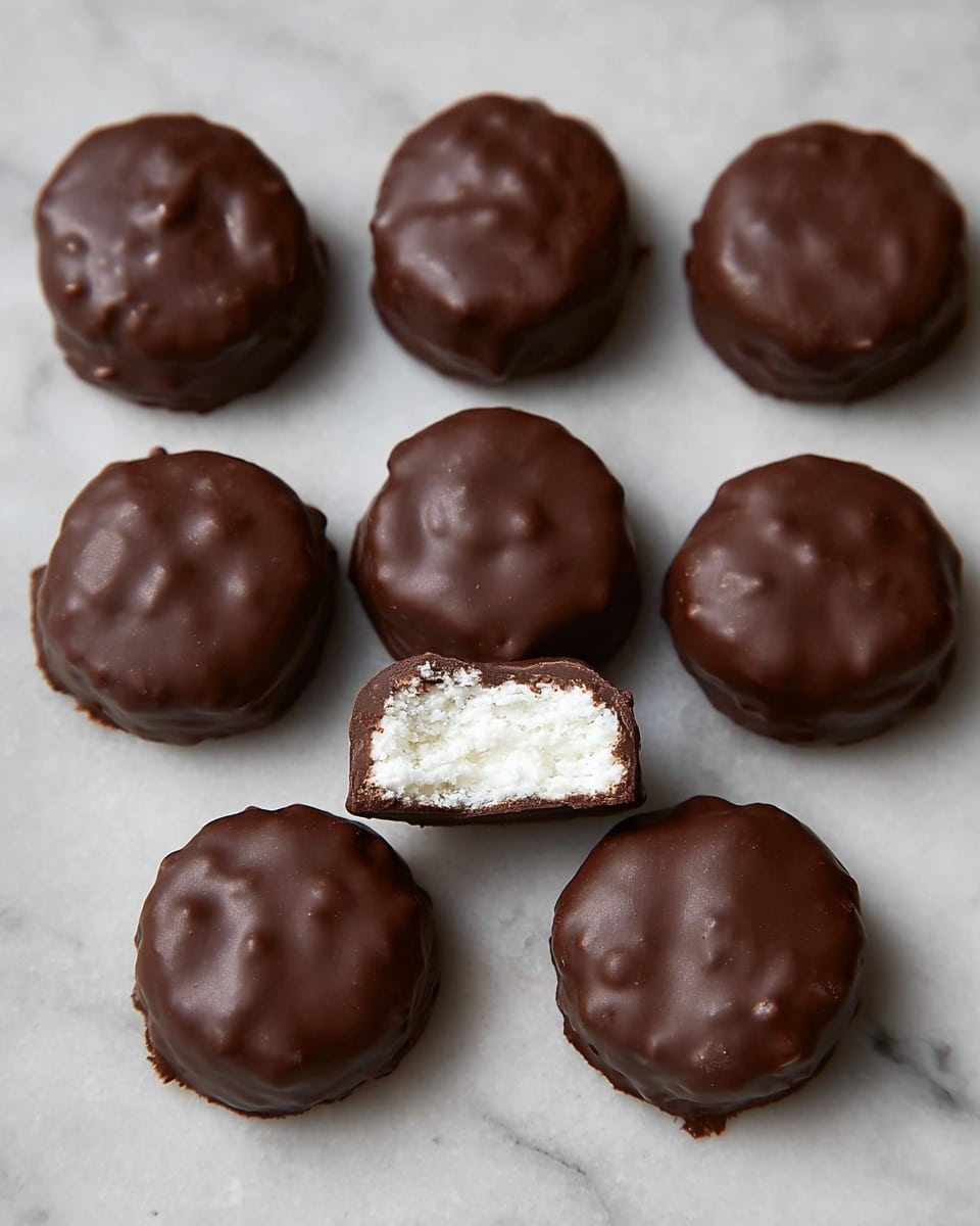 The image shows nine chocolate-coated round treats arranged in three rows on a white marbled surface. The first two rows each have three whole treats with a shiny, smooth dark brown chocolate outer layer. The front row has three treats, with the middle one bitten in half, revealing a soft, white, crumbly filling inside, while the other two remain whole and glossy. The texture of the chocolate coating is slightly uneven, showing small lumps and gentle waves. photo taken with an iphone --ar 4:5 --v 7
