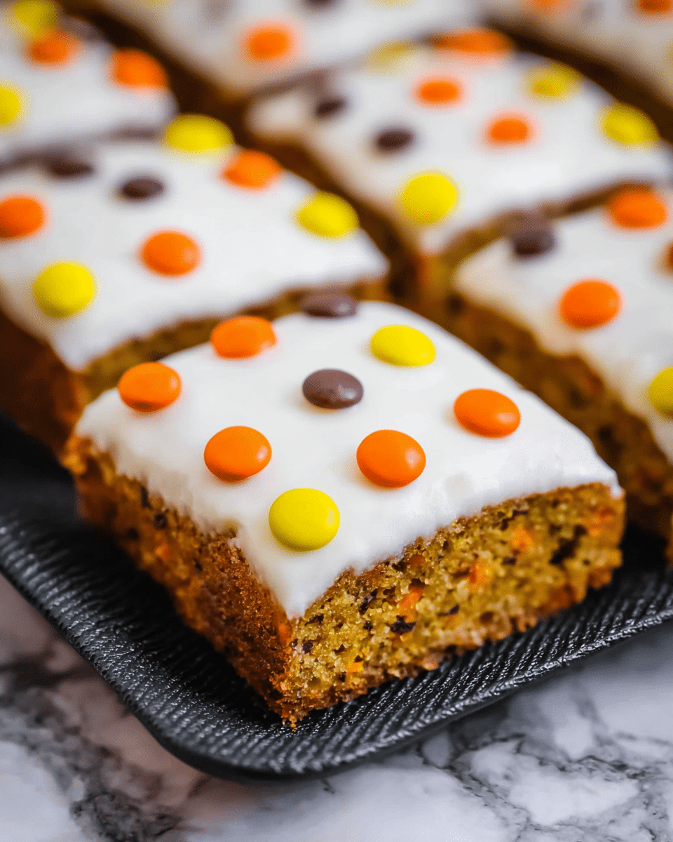 A close-up view of square carrot cake pieces arranged closely on a black textured tray, each piece having two visible layers: a dense, moist orange-brown cake base with tiny specks and a thick, smooth white frosting layer on top. The frosting is decorated with small round candy pieces in bright yellow, orange, and brown colors scattered evenly across each slice. The tray is placed on a white marbled surface with subtle grey veins. Photo taken with an iphone --ar 4:5 --v 7