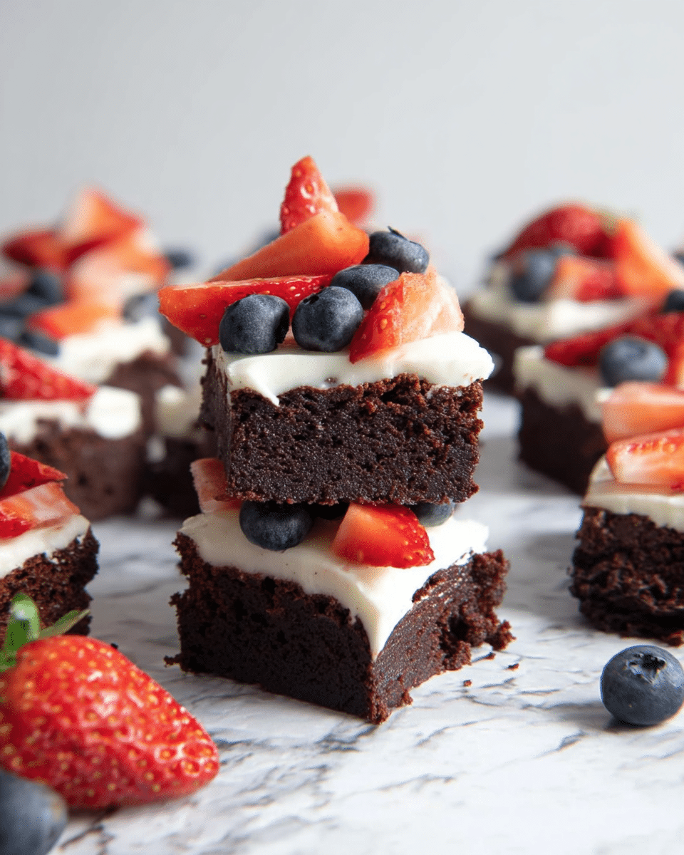 The image shows small square pieces of dark brown, moist chocolate brownies placed on a white marbled textured surface. Each brownie has a thick layer of white whipped cream on top, which looks soft and smooth. On the whipped cream layer, there are fresh, bright red strawberry slices and round, deep blue blueberries arranged neatly. Some blueberries are scattered around the brownies on the surface, along with two long, thin, dark brown vanilla pods crossing each other near the bottom right. In the top left corner, a white bowl with a blue rim contains more whipped cream. The overall look is colorful with the dark brownies, white cream, and fresh fruit on a clean white marbled background. photo taken with an iphone --ar 4:5 --v 7