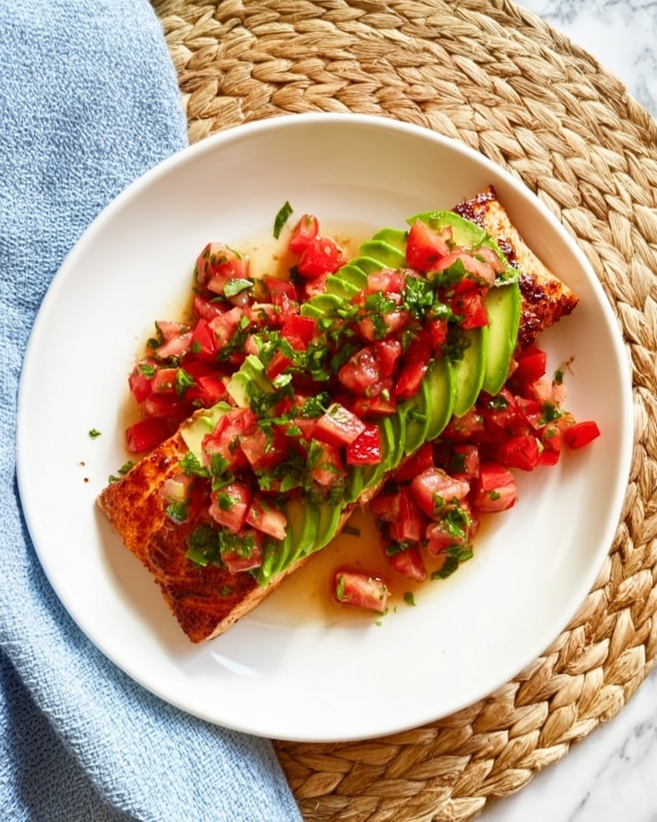 A white plate shows a grilled salmon fillet as the base layer, its texture crispy and golden brown on the sides. On top of the salmon, there is a layer of bright green avocado slices, smooth and neatly arranged. The top layer consists of small chunks of fresh red tomatoes mixed with finely chopped green herbs, adding a fresh and colorful touch. Extra tomato and herb pieces are scattered around the salmon on the plate. The plate sits on a woven, light tan placemat with a soft blue cloth nearby, all on a white marbled surface. photo taken with an iphone --ar 4:5 --v 7