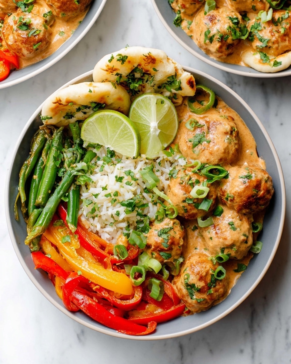 The image shows a white bowl filled with a colorful dish arranged in layers. At the bottom, there are cooked green beans and red and yellow bell pepper slices, creating a bright, fresh base with a mix of green, red, and yellow colors. On top of these vegetables, there are round brown meatballs coated in a rich, creamy light orange sauce. The sauce gently covers the meatballs and some vegetables. On one side of the bowl, there is a small mound of white rice mixed with chopped green herbs, providing a soft, fluffy texture. Next to the rice, there are two lime wedges with a pale green color placed casually. On the edge of the bowl, some pieces of soft, slightly browned naan bread are partially visible, sprinkled with green herbs. The dish is garnished with thinly sliced green onions and chopped fresh cilantro, which add pops of green and freshness. The bowl sits on a white marbled surface, and the photo is taken with an iphone --ar 4:5 --v 7