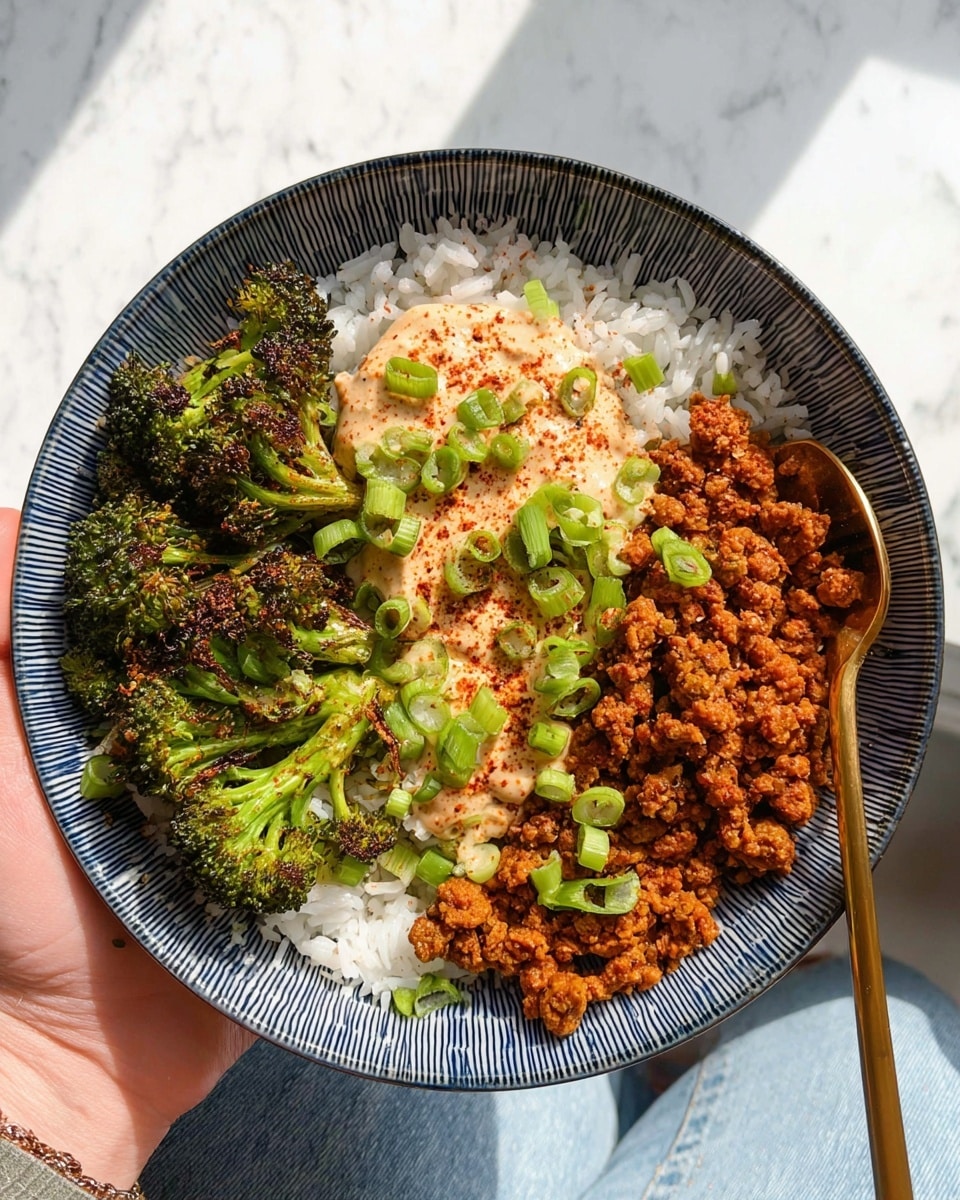 A bowl with three main layers is held by a woman's hand over a white marbled texture. The bottom layer is white rice with a slightly sticky texture. On one side, bright green broccoli pieces with a slightly crispy look are placed. On the other side, a browned, crumbly textured mixture that appears to be spiced ground meat or plant-based crumble adds a warm orange-brown color. In the center, a creamy, light pinkish sauce topped with a sprinkle of red spice is spread, with small green chopped scallions sprinkled over the dish. A golden spoon is resting inside the bowl near the spiced mixture. Photo taken with an iphone --ar 4:5 --v 7