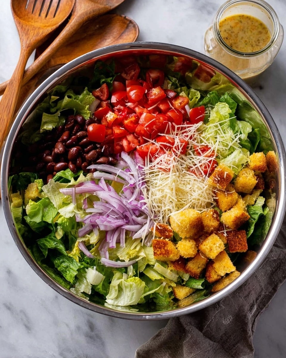 A large metal bowl filled with a colorful salad sits on a white marbled surface. The salad is made in layers with green lettuce at the bottom, bright red chopped tomatoes on the left side, chopped dark brown beans near the top, and thin slices of red onion mixed in. On the right side, there are golden yellow croutons sprinkled with white shredded cheese. A glass jar of dressing leans against the side of the bowl. Wooden salad spoons are placed nearby. The overall look is fresh and inviting. photo taken with an iphone --ar 4:5 --v 7