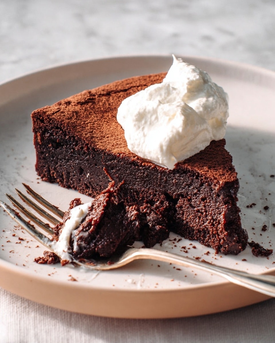 A single slice of rich, dark chocolate cake with a moist and dense texture sits on a white plate, its top layer slightly cracked and dry-looking. The cake is topped with a soft dollop of white whipped cream. Beside the slice, there is a silver fork with some cake crumbs and whipped cream stuck to it. The plate rests on a white marbled texture surface. Photo taken with an iphone --ar 4:5 --v 7