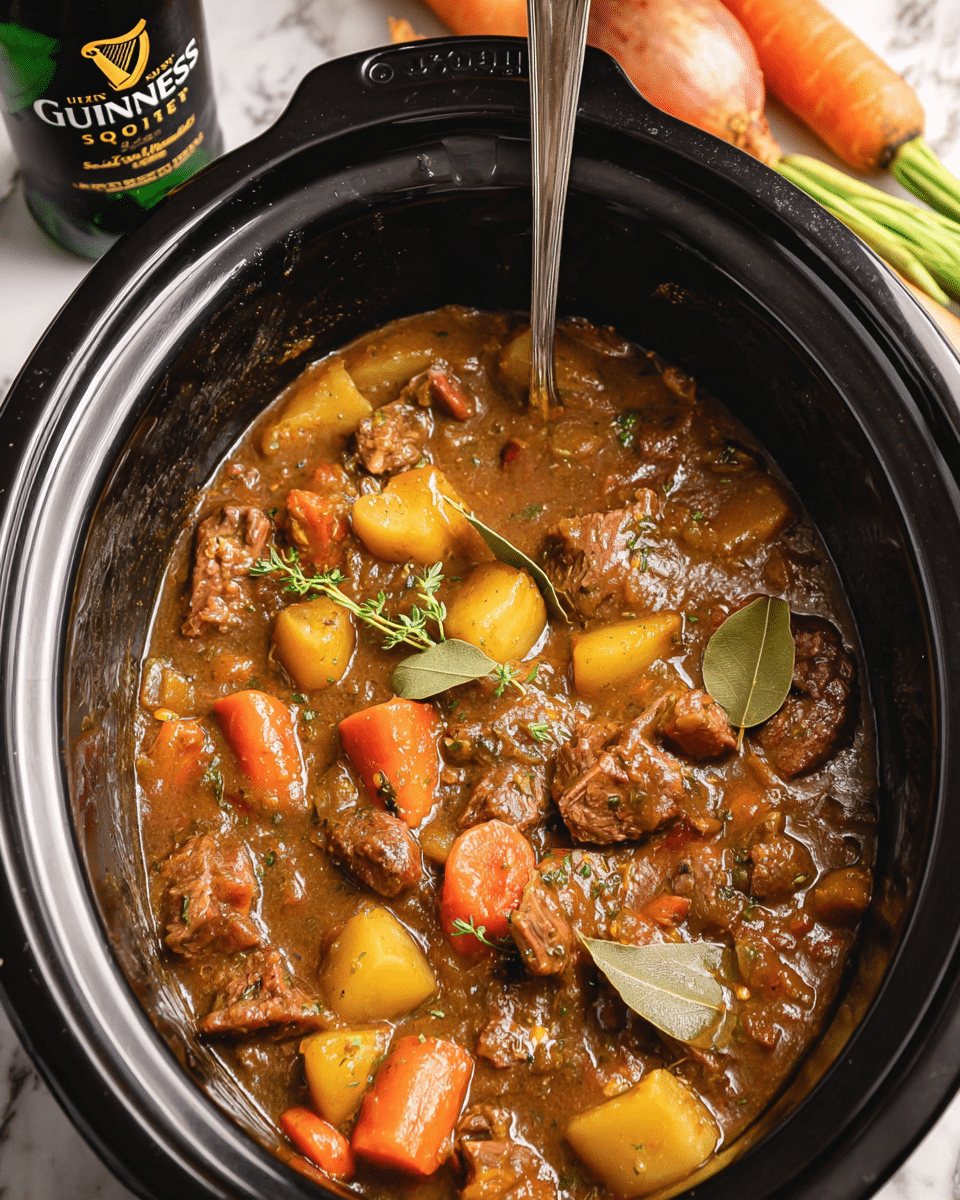 A close-up view of a black slow cooker filled with a thick brown stew with visible chunks of tender beef, bright orange carrot slices, and yellowish potato pieces; bay leaves and small sprigs of fresh thyme float on top, adding green hues and texture. The stew looks rich and glossy with a smooth sauce covering the ingredients. A silver spoon rests inside the cooker, standing upright. Around the cooker are fresh whole vegetables—carrots and an onion—and a bottle of Guinness Original Extra Stout, all placed on a white marbled surface. photo taken with an iphone --ar 4:5 --v 7