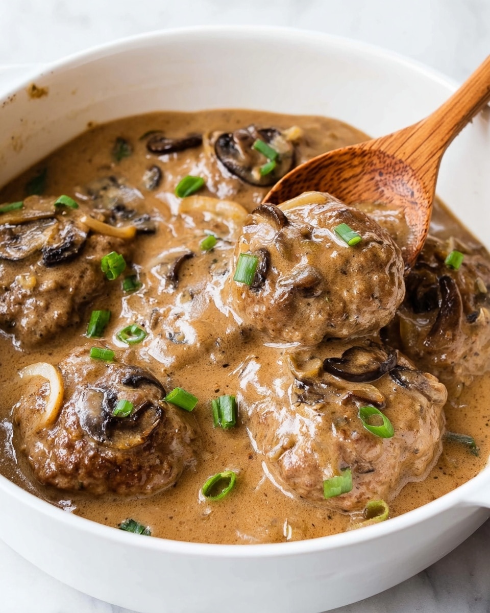 The image shows a white bowl filled with a brown sauce containing four meat patties. The patties are covered with a creamy brown gravy that has visible slices of light brown onions and dark brown mushrooms scattered throughout. Small pieces of chopped green onions add a pop of color on top. A wooden spoon with a smooth texture is partially dipped into the sauce, lifting one of the patties slightly. The bowl sits on a white marbled surface. photo taken with an iphone --ar 4:5 --v 7