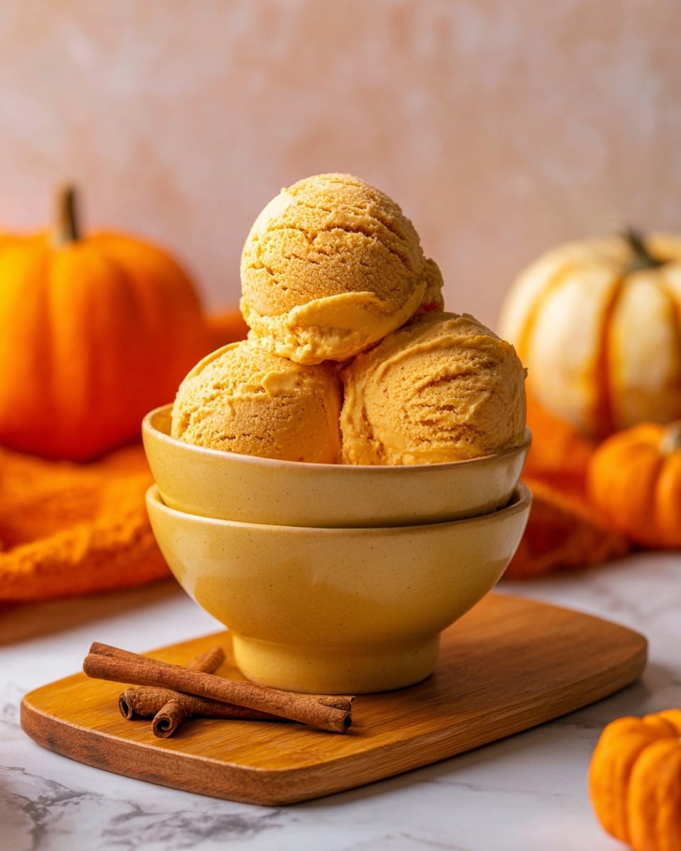 Three scoops of orange pumpkin ice cream with a creamy, slightly rough texture are stacked in a single yellow ceramic bowl that sits on top of an identical bowl. The bowls rest on a wooden board placed on a white marbled surface. Around them, there are whole pumpkins and two cinnamon sticks lying nearby, adding warm color tones to the scene. The background is softly blurred with a light orange tone. photo taken with an iphone --ar 4:5 --v 7