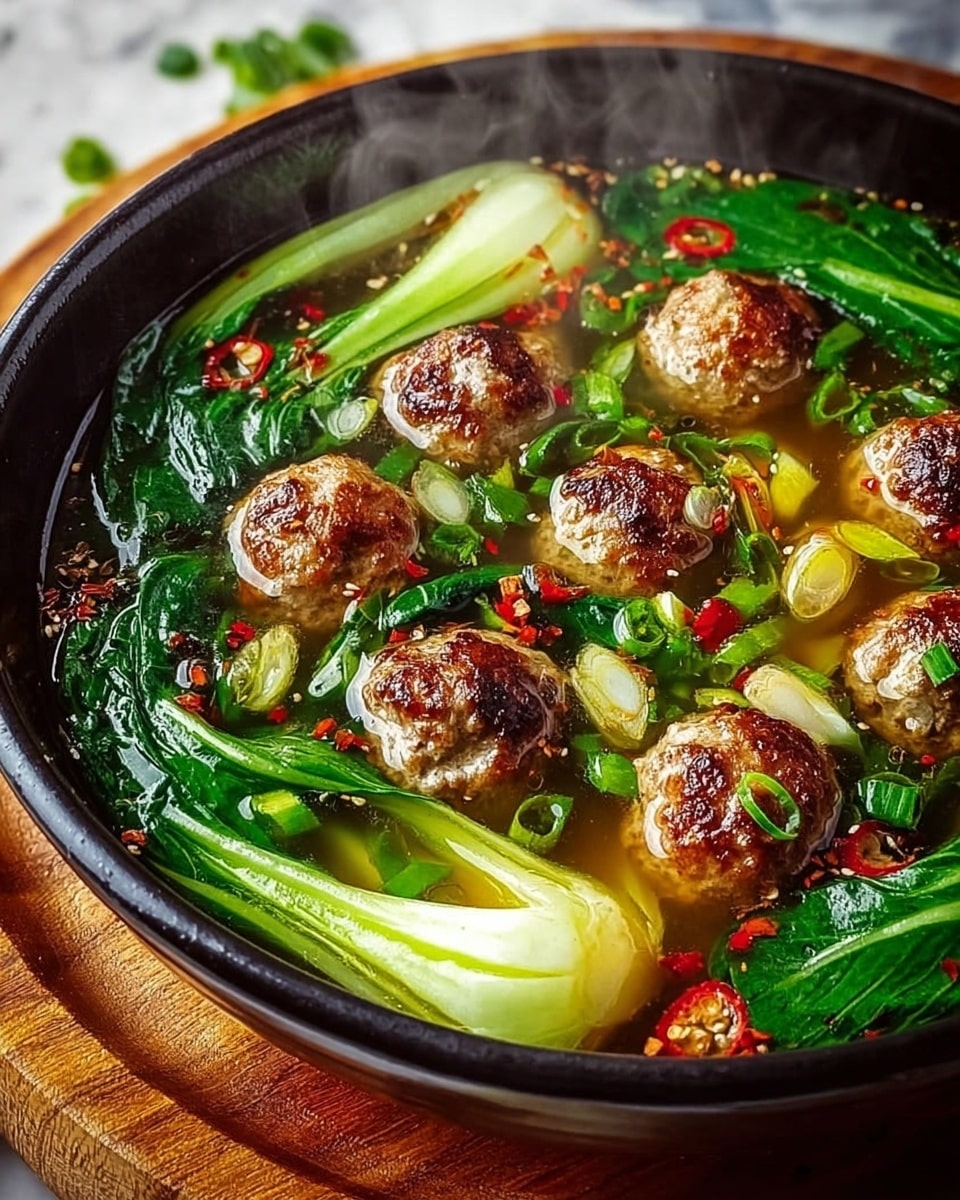 A close-up of a black bowl filled with clear golden broth, inside are about eight browned meatballs floating evenly. There are bright green leafy bok choy pieces arranged in layers around and beneath the meatballs, with white stalks visible. Thin slices of green onions and small red chili flakes are scattered on the surface, adding color contrast. Steam rising shows the dish is hot and fresh, placed on a round wooden board over a white marbled surface. photo taken with an iphone --ar 4:5 --v 7