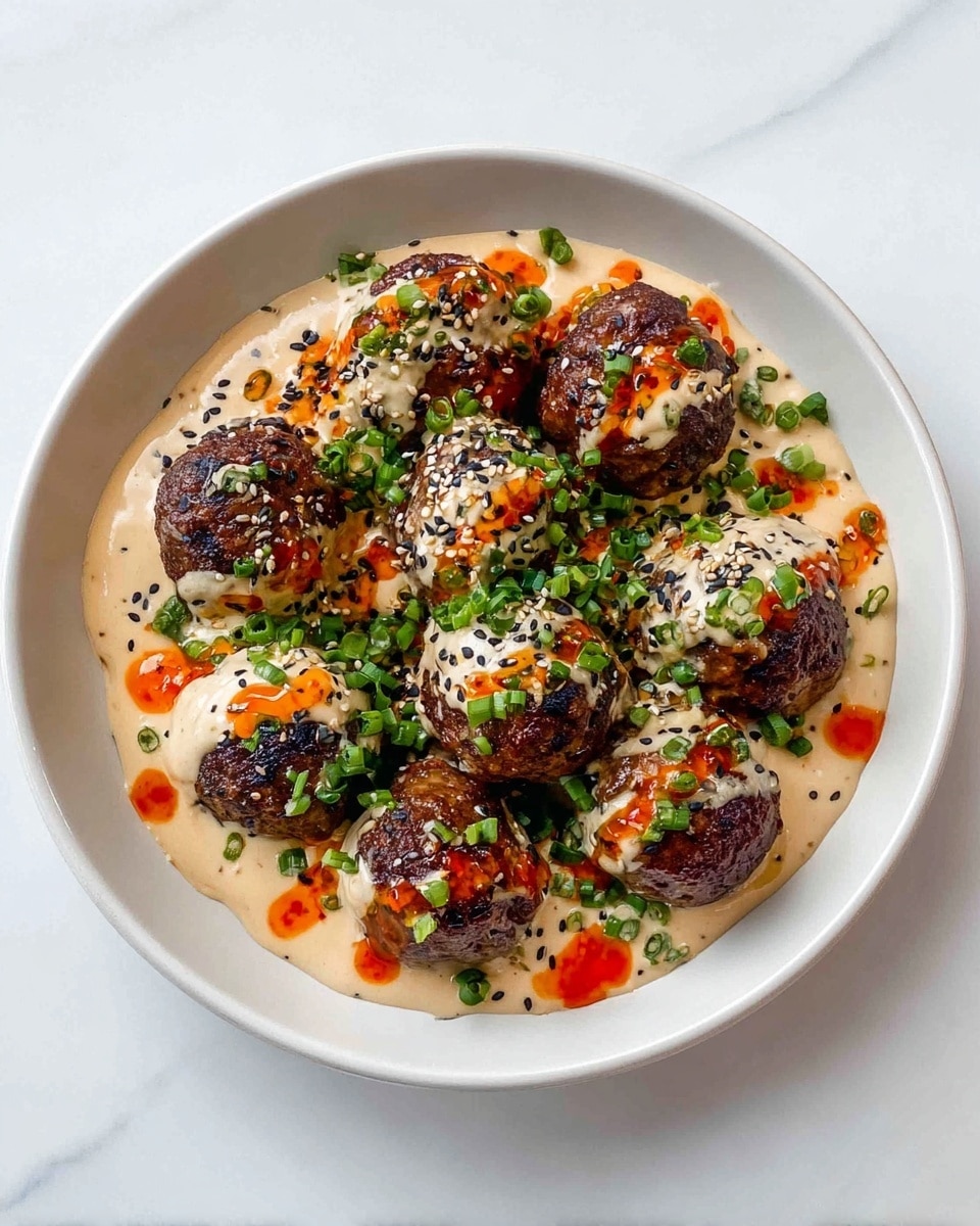 The dish shows a white round plate filled with about ten browned meatballs as the base layer, each having a glossy texture from cooking. The second layer is a creamy light beige sauce generously draped over the meatballs, with some bright red-orange chili oil drizzled unevenly on top. Scattered black sesame seeds and finely chopped green onions cover the sauce, adding color contrast and texture. The plate sits on a white marbled surface, and the overall look is vibrant with a mix of smooth, glossy, and fresh green details. Photo taken with an iphone --ar 4:5 --v 7