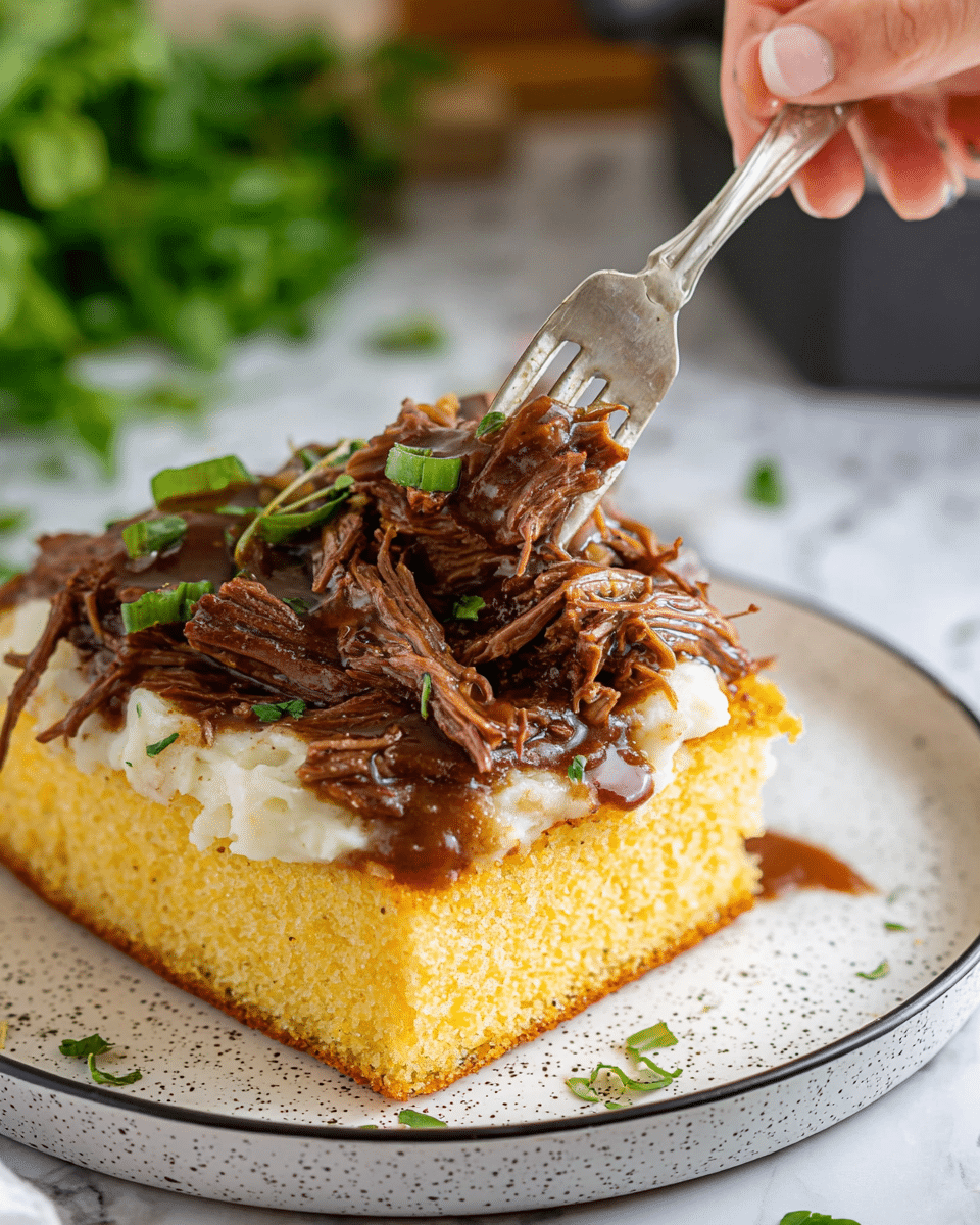 A close-up of a dish with three layers on a white plate with black speckles and a thin black rim. The bottom layer is a thick slice of golden brown cornbread with a slightly rough texture. The middle layer is a smooth, creamy white mashed potato spread evenly over the cornbread. The top layer consists of dark brown shredded beef in a glossy gravy, garnished with small green herb pieces. A fork held by a woman's hand is pressing into the beef, causing some gravy to drip over the cornbread. The background shows a white marbled surface with some leafy greens nearby. Photo taken with an iphone --ar 4:5 --v 7