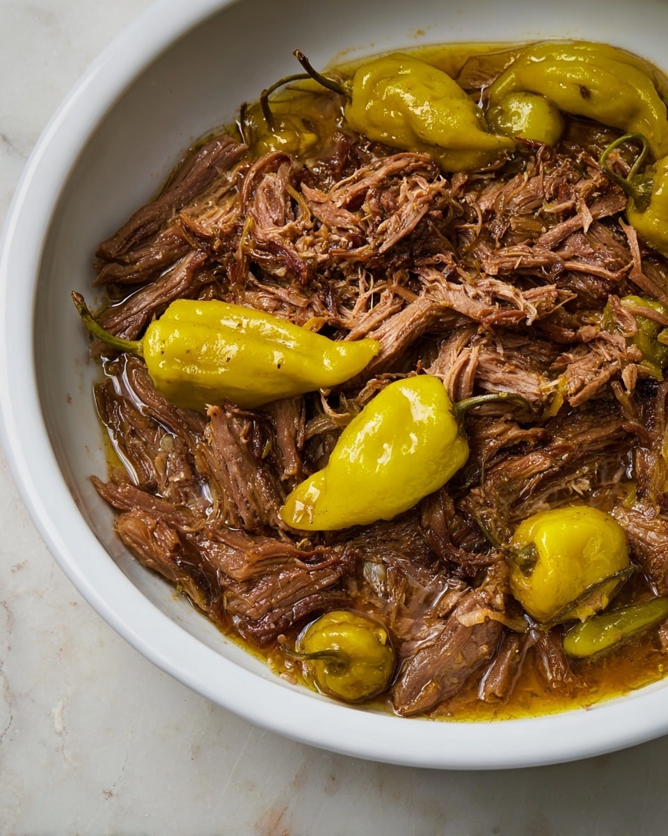 The dish shows a close-up of shredded brown meat mixed with a glossy, oily sauce, giving it a moist and tender look. Scattered among the meat are several whole yellow-green peppers with smooth, slightly wrinkled skins and stems still attached. All the ingredients sit inside a large white bowl with a clean, simple edge, and the bowl is placed on a white marbled textured surface. The focus captures the shimmer of the sauce and the texture of both the meat and peppers. photo taken with an iphone --ar 4:5 --v 7