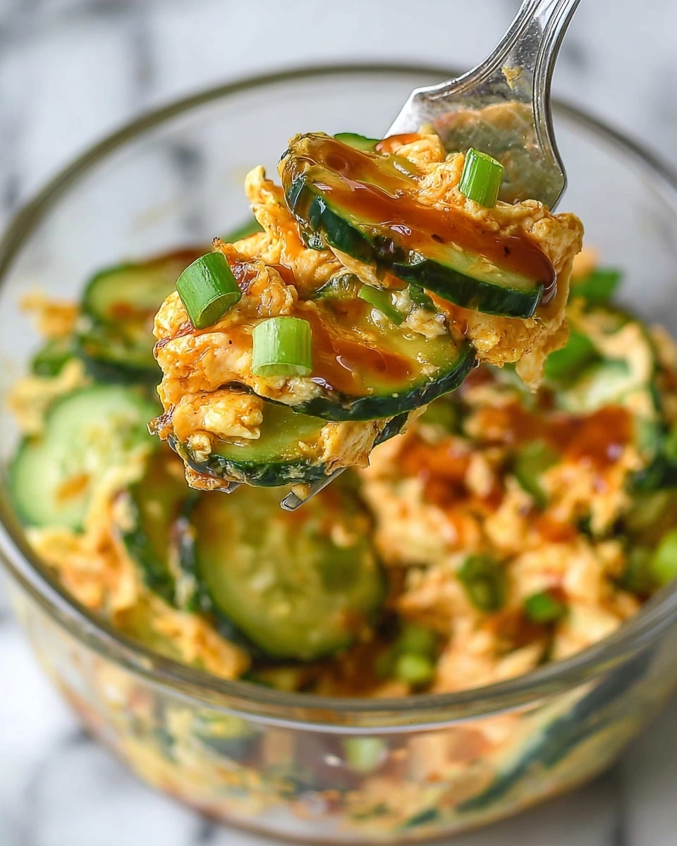 A close-up view of a fork holding a mix of creamy scrambled eggs layered with thin, green cucumber slices that have a slightly cooked texture, topped with chopped green onions and a glossy drizzle of reddish-brown sauce. In the background, a clear glass bowl contains the same mixed dish with visible layers of scrambled eggs and cucumbers, all resting on a white marbled surface. The colors include bright yellow-orange from the eggs, fresh green from the cucumbers and onions, and the shine of the sauce on top, creating a vibrant and fresh look. Photo taken with an iphone --ar 4:5 --v 7