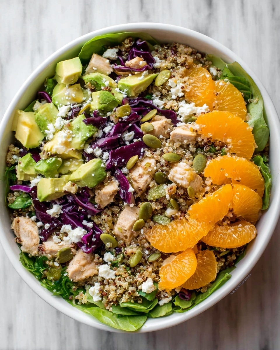 A bowl filled with a colorful salad that has a base layer of green leaves around the edges, topped with a mix of beige quinoa grains, small green avocado chunks, orange mandarin slices, purple cabbage strips, and small pieces of cooked chicken that are light brown. There are also scattered white crumbles of cheese and green pumpkin seeds on top, all sitting inside a white bowl placed on a white marbled surface. photo taken with an iphone --ar 4:5 --v 7