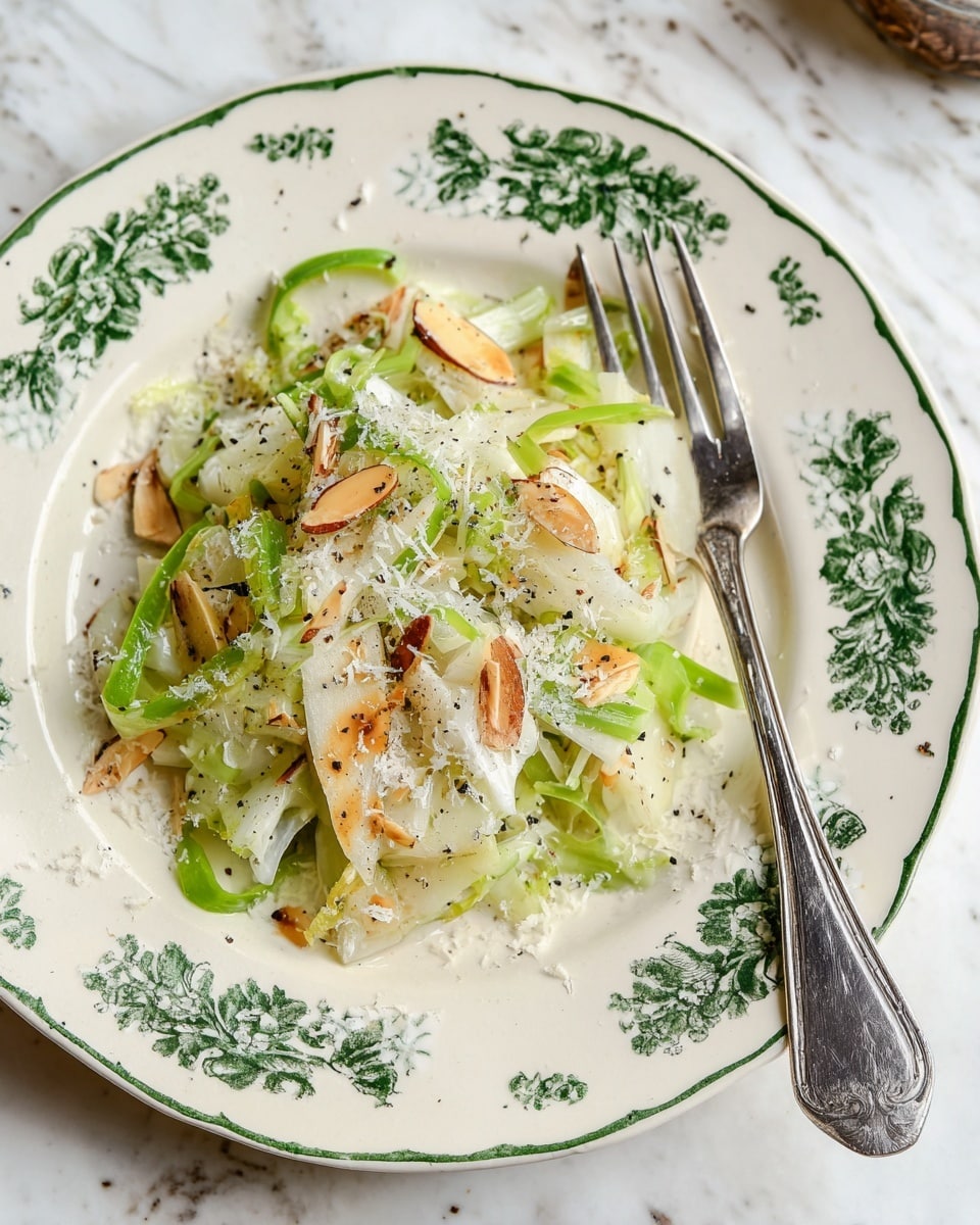 A white plate with green floral patterns holds a fresh salad with multiple layers, starting with thin, pale green slices of celery and fennel on the bottom. On top, there are toasted almond slivers with a light brown, slightly charred texture scattered evenly. The dish is topped with finely grated white cheese and small specks of black pepper, along with thin slices of bright green ribbons. A silver fork rests on the right side of the plate, on a white marbled surface. photo taken with an iphone --ar 4:5 --v 7