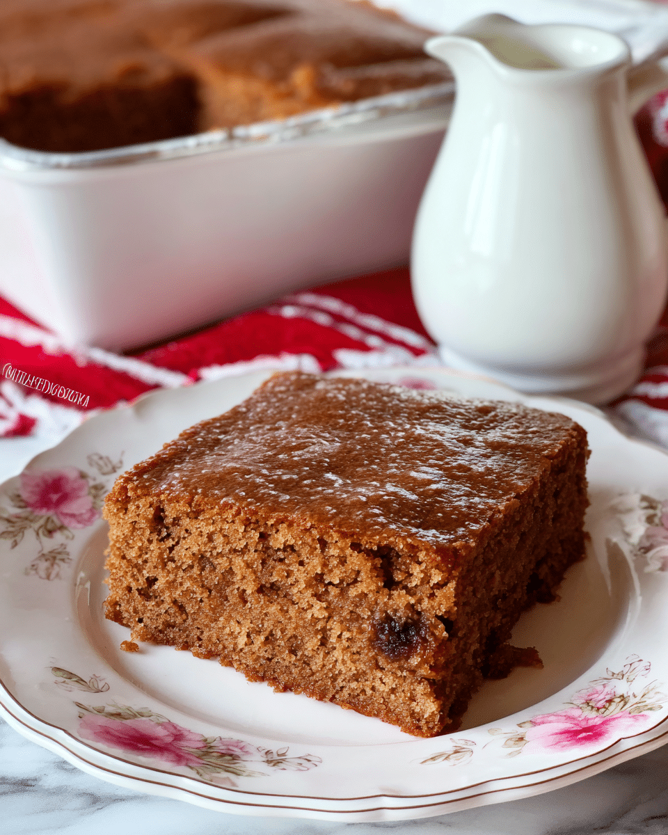 A single square piece of moist, brown cake with a slightly shiny surface sits on a white plate with pink floral designs around the edge. The cake looks soft and spongy, showing small air holes and a dense texture, with bits of darker filling visible near the bottom layer. Behind the plate, there is a white jug with a rounded spout, and to the left, a larger baking pan contains more of the same cake. All items are set on a white marbled surface with a red and white striped cloth partially visible underneath. photo taken with an iphone --ar 4:5 --v 7