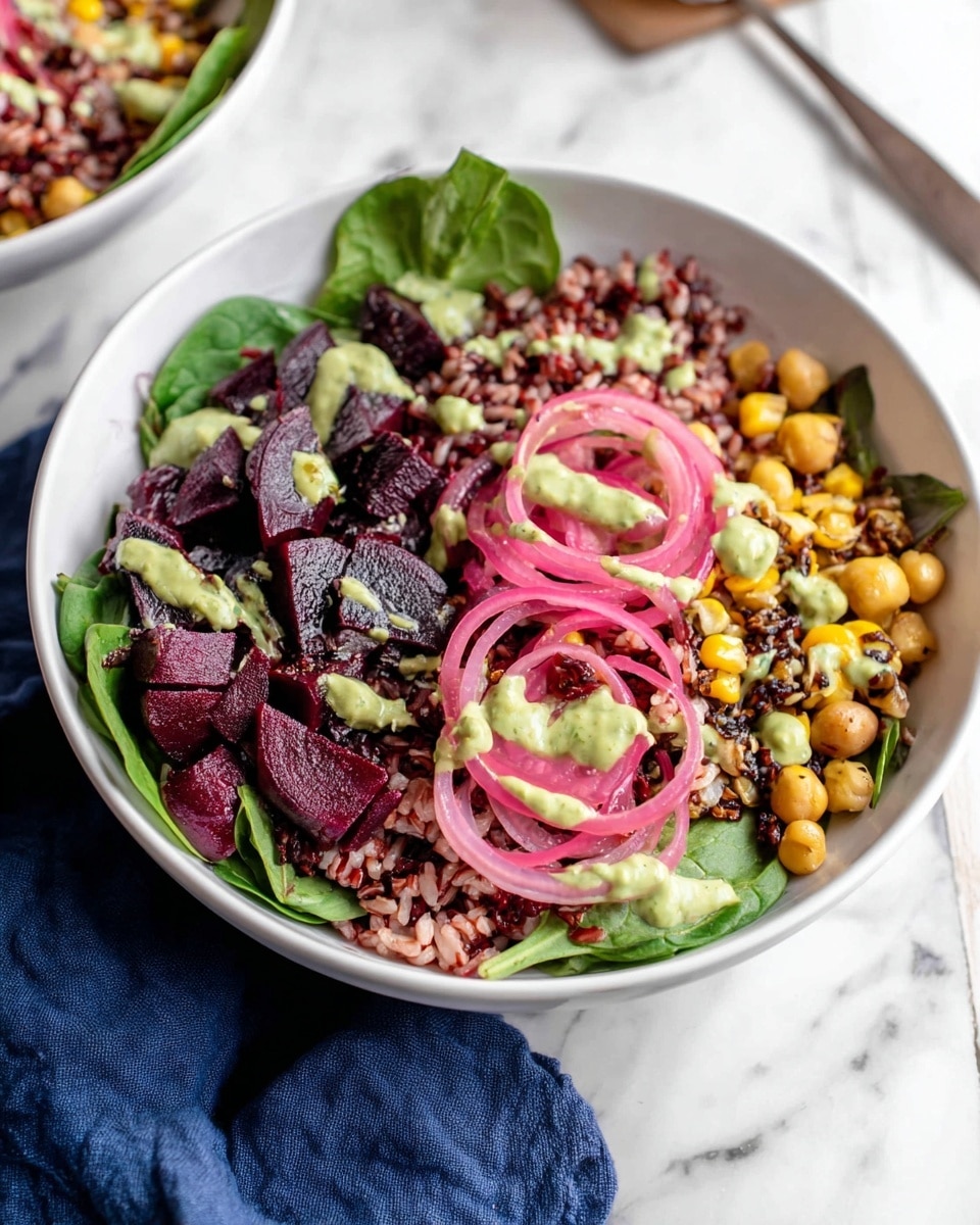 A white bowl holds a fresh salad with distinct layers. The bottom layer is bright green spinach leaves. On top, there are dark purple roasted beet slices arranged mostly on one side. Scattered across the bowl are yellow corn kernels and light brown chickpeas mixed with red rice, giving a grainy texture. Garnishing the salad are thin rings of pickled pink onions and a drizzle of creamy green dressing. The bowl sits on a white marbled surface with a dark blue cloth nearby. Photo taken with an iphone --ar 4:5 --v 7