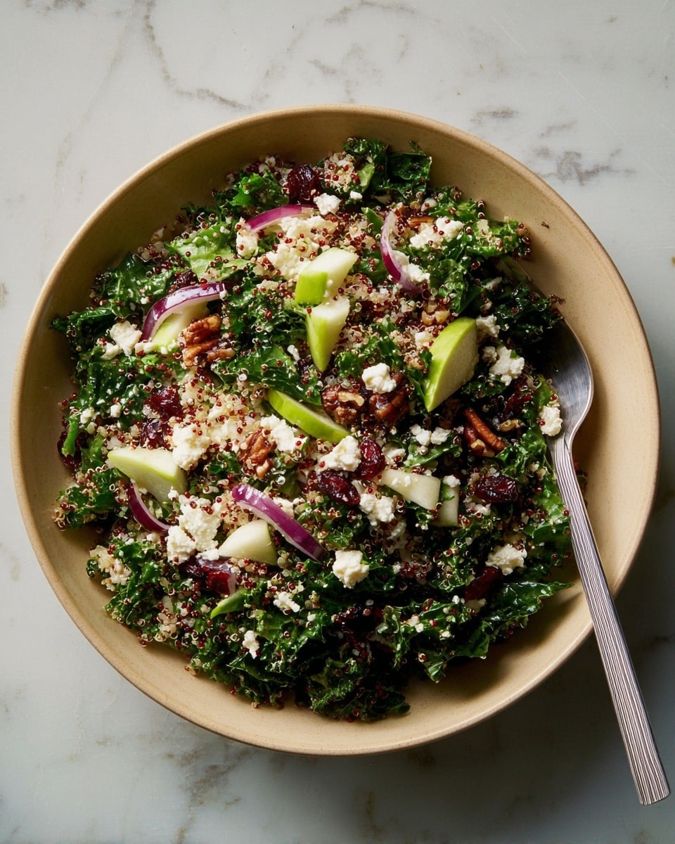A beige bowl filled with a colorful salad on a white marbled surface, showing layers of dark green kale leaves as the base, topped with small pieces of red and white quinoa scattered evenly throughout. There are bright green apple chunks and thin strips of pale purple-red onion mixed in, along with white crumbles of cheese dotted on top. Dark brown pecan nuts and dark red dried cranberries are spread across the salad, adding texture and color contrast. A silver fork rests inside the bowl on the right side. photo taken with an iphone --ar 4:5 --v 7