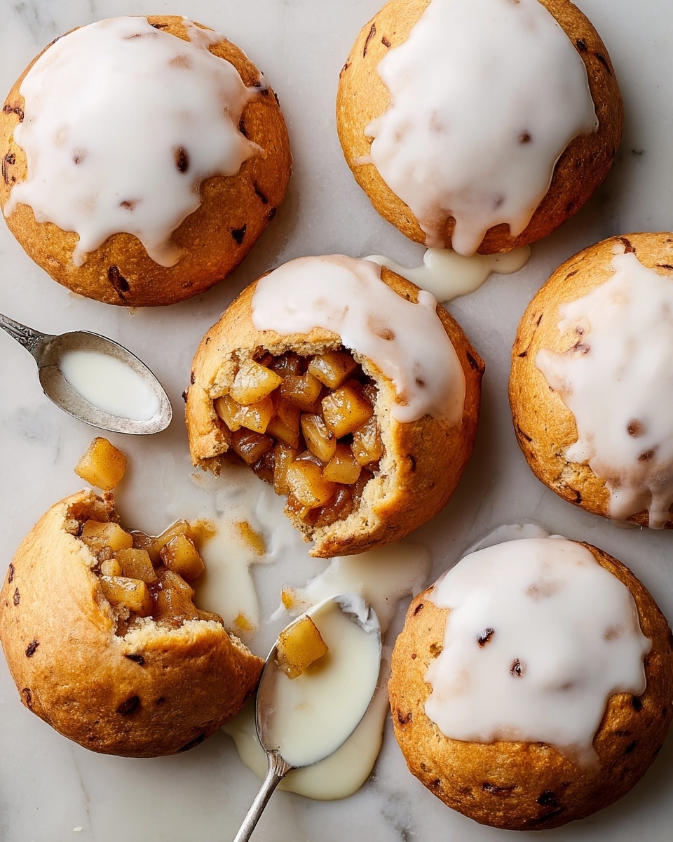 A top view of six round golden brown pastries on a white marbled surface, each with a slightly uneven texture and small dark spots. Three pastries are topped with smooth white glaze that covers about half of their surfaces. One pastry in the center is broken open to show a filling of small, soft, light brown apple pieces with a shiny coating spilling out. A silver spoon with white glaze rests near the pastries with some glaze spilled next to it. photo taken with an iphone --ar 4:5 --v 7
