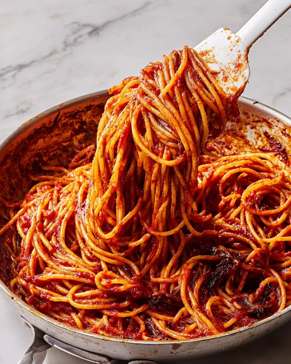 A close-up view of a large amount of spaghetti pasta coated in red tomato sauce with burnt edges, lifted with a white spatula that has some sauce stains; the spaghetti is thick, cylindrical, and clumped, showing both smooth and slightly charred textures. The scene is set against a white marbled texture background and the pasta is in a large pan with reddish-brown residue around the sides. photo taken with an iphone --ar 4:5 --v 7