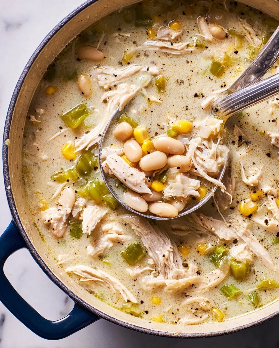 A close-up view of a creamy chicken soup in a dark blue pot showing one woman's hand holding a silver ladle lifting a scoop. The soup has layers of light beige broth with textures of shredded white chicken pieces, small white beans, yellow corn kernels, diced green bell peppers, and bits of onion mixed throughout. The surface of the soup has small bubbles, droplets of oil, and sprinkled black pepper. The pot edge and handle are visible on the right side, set against a white marbled texture background. photo taken with an iphone --ar 4:5 --v 7