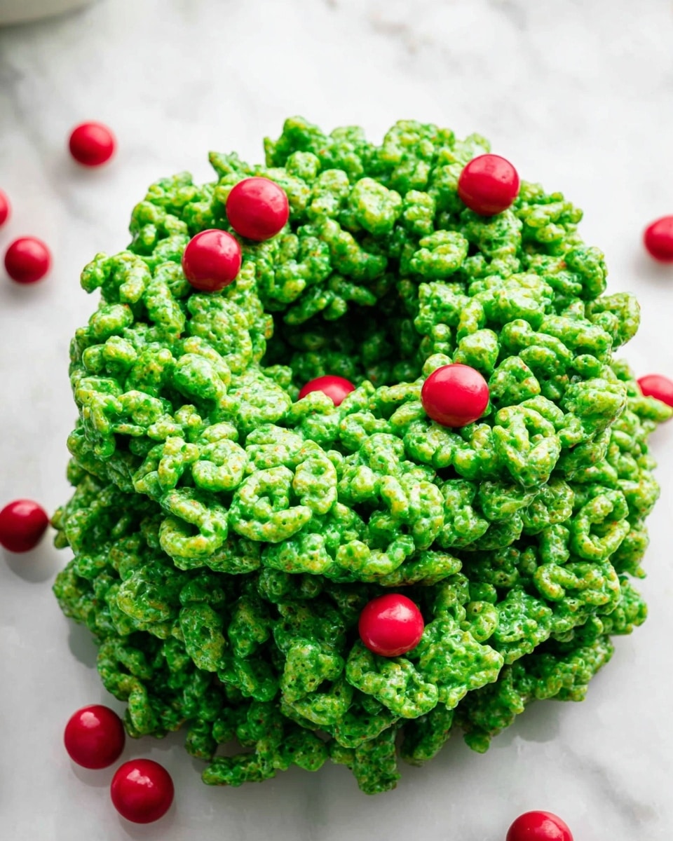 A tall stack of green cereal treats shaped like a Christmas wreath sits on a white marbled surface, each layer made of bright green cereal clusters tightly packed together showing a shiny, sticky texture. Scattered around the wreath are small, round, bright red candy balls, adding contrast and a festive touch. The wreath has an open circular center and uneven edges from the cereal pieces sticking out at different angles. photo taken with an iphone --ar 4:5 --v 7