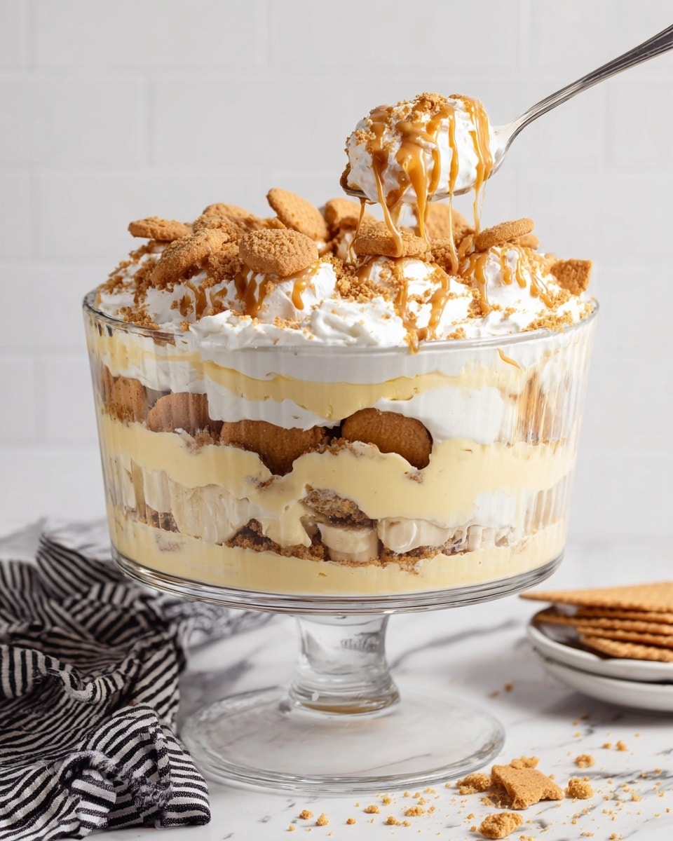 A clear glass trifle bowl on a tall pedestal contains five visible layers: the bottom layer has light tan wafer cookies, followed by a thick layer of creamy pale yellow pudding. Above this is another layer of wafer cookies with banana slices evenly placed on top. Next comes a thick white whipped cream layer, topped with crumbled wafer cookies and light brown peanut butter drizzle. A spoon holding a scoop of the trifle shows all the layers mingled together with the peanut butter lines and whipped cream fluffy texture clearly visible. The bowl sits on a white marbled surface with a black and white striped cloth nearby and some scattered wafer crumbs around. Photo taken with an iphone --ar 4:5 --v 7