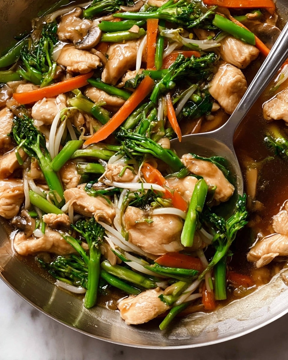 The image shows a close-up of a stir-fry dish with layers of light tan cooked chicken pieces scattered throughout. Bright green stalks of broccoli or similar greens and long green beans are mixed with thin orange carrot slices and white bean sprouts. Sliced white mushrooms are visible among the vegetables, all coated in a shiny light brown sauce that pools slightly at the bottom. The food is inside a shiny metal pan on a white marbled surface, with a metal spoon partly visible, mixing the ingredients. photo taken with an iphone --ar 4:5 --v 7