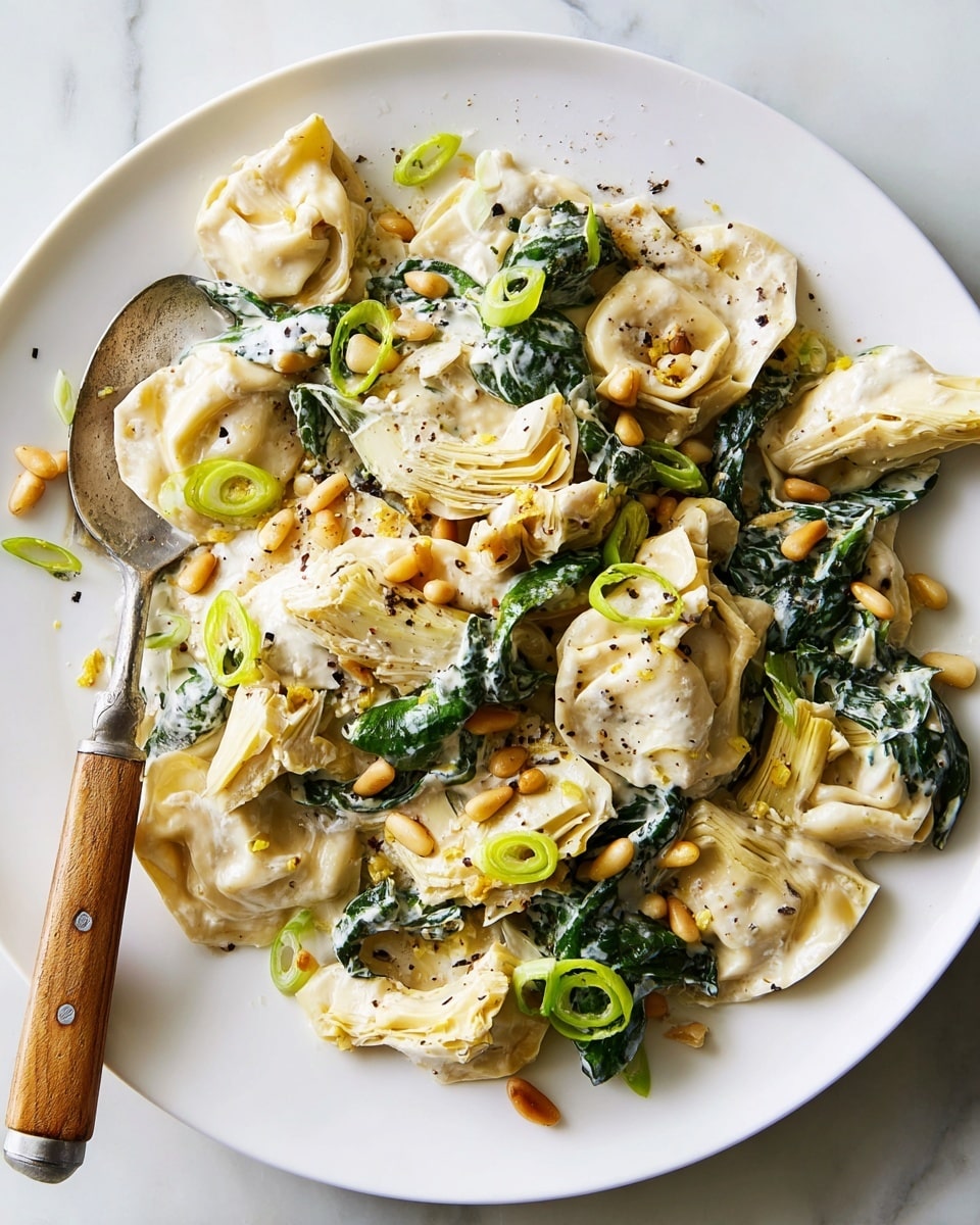 A close-up view of a creamy pasta dish inside a white bowl with a black rim, featuring several pieces of folded tortellini and ravioli coated with a smooth white sauce. Scattered on top are light brown toasted pine nuts, thinly sliced bright green scallions, and specks of black pepper. Fresh spinach leaves add a touch of dark green, while pale yellow artichoke hearts provide soft texture. The dish is finished with a sprinkle of finely grated lemon zest over the layers, all resting on a white marbled surface. Photo taken with an iphone --ar 4:5 --v 7