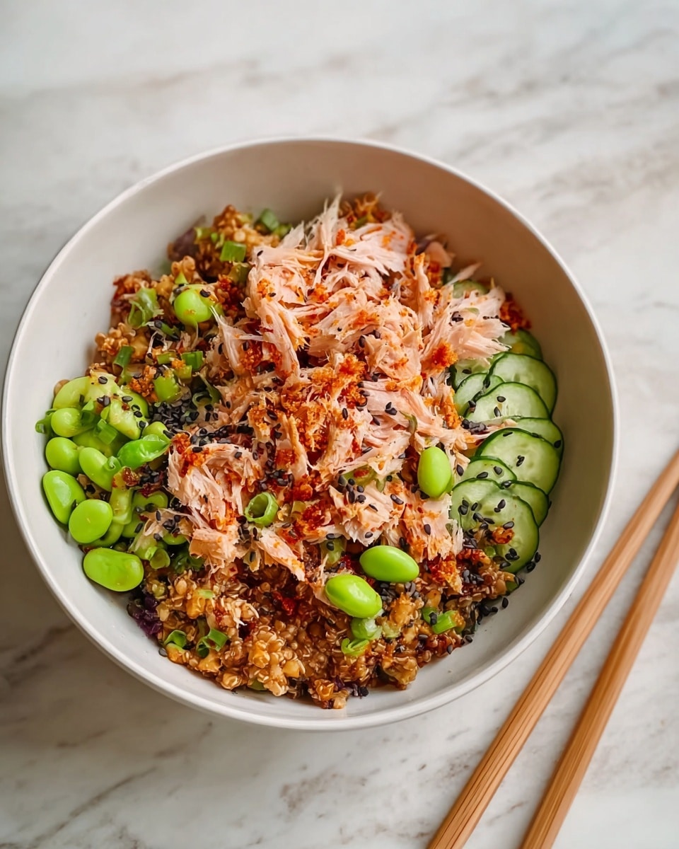 A white bowl filled with a colorful mixed dish with about three main layers: at the bottom is a grain layer in brown with a slightly sticky texture, topped with scattered bright green edamame and slices of crisp cucumber, and finally a generous layer of shredded light pink shredded fish mixed with bits of orange-red spices and black sesame seeds sprinkled around. The bowl sits on a white marbled surface with wooden chopsticks placed to the right side. photo taken with an iphone --ar 4:5 --v 7