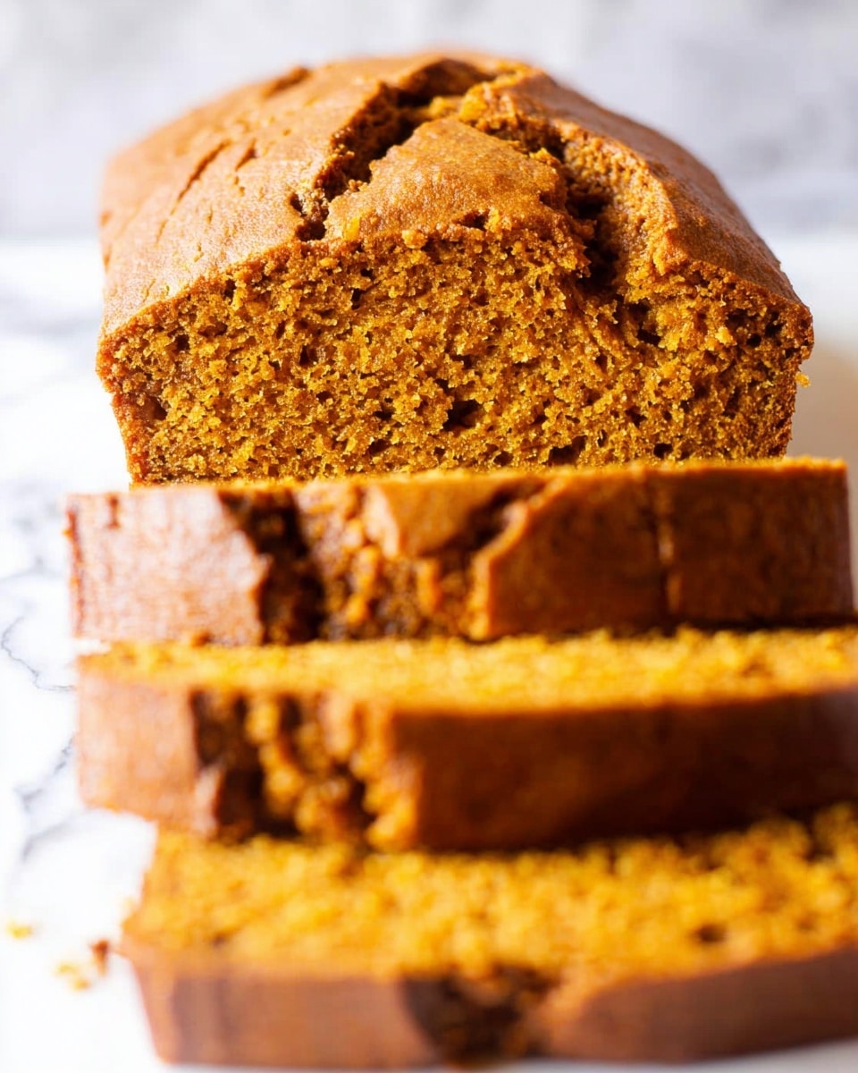 A loaf of moist pumpkin bread is shown close up, cut into several thick slices. The bread has a rough, golden brown crust on top with natural cracks, while the inside is a soft, dense orange-brown crumb with a slightly grainy texture. The slices are stacked slightly out of focus in front of the main loaf, which is centered in the image. The background is a white marbled texture. Photo taken with an iphone --ar 4:5 --v 7