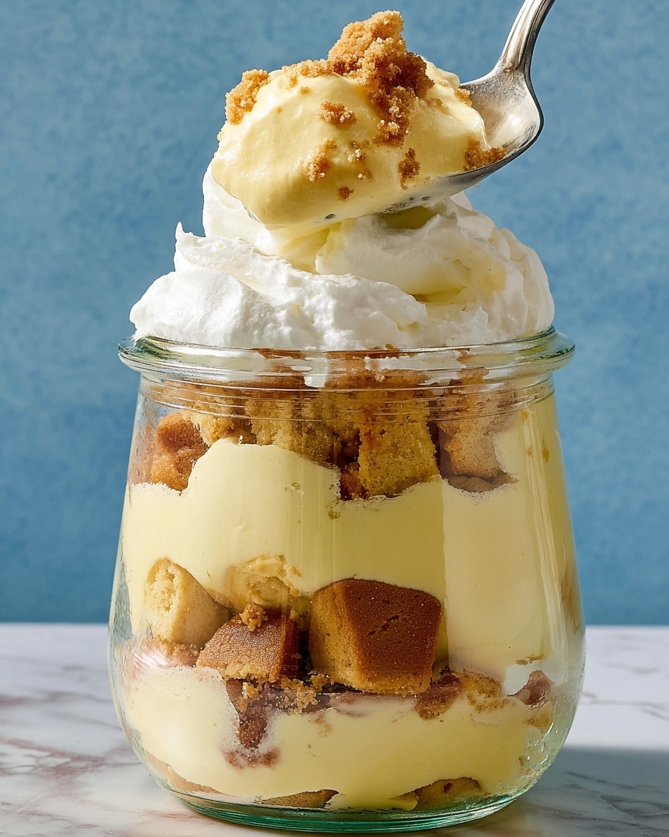 A clear glass jar filled with four layers of a creamy yellow pudding and crumbled light brown cookie pieces mixed within each layer. The bottom layer consists mostly of cookie chunks, followed by a thick layer of smooth pudding. Above that is another layer of mixed cookie crumbs and pudding, topped with a fluffy white whipped cream layer. A spoon at the top holds a scoop of pudding and cookie crumbs, with the whipped cream slightly melting over the edges. The background is a soft blue, and the jar sits on a white marbled texture. photo taken with an iphone --ar 4:5 --v 7
