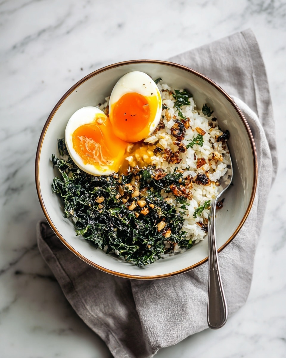 A bowl with three main layers: the bottom layer is chopped dark green kale, the middle layer is white rice mixed with small brown toasted bits, and the top layer is a halved soft-boiled egg with a bright orange yolk slightly runny, placed on top, leaning slightly to the side. The bowl is white with a thin brown rim, sitting on a soft, light gray cloth on a white marbled surface. A silver spoon is partially inside the bowl on the right side. photo taken with an iphone --ar 4:5 --v 7