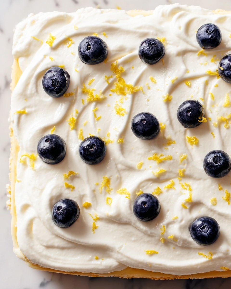 A close-up of a dessert with a smooth, thick white cream layer spread evenly across the top, featuring soft swirls and gentle peaks. Scattered on the cream are whole, plump blueberries, each dark blue with some slight natural shine and texture, and small pieces of bright yellow lemon zest sprinkled lightly over the surface, adding color contrast. The dessert rests on a thin, pale yellow base, visible beneath the creamy layer. The background is a white marbled texture. photo taken with an iphone --ar 4:5 --v 7