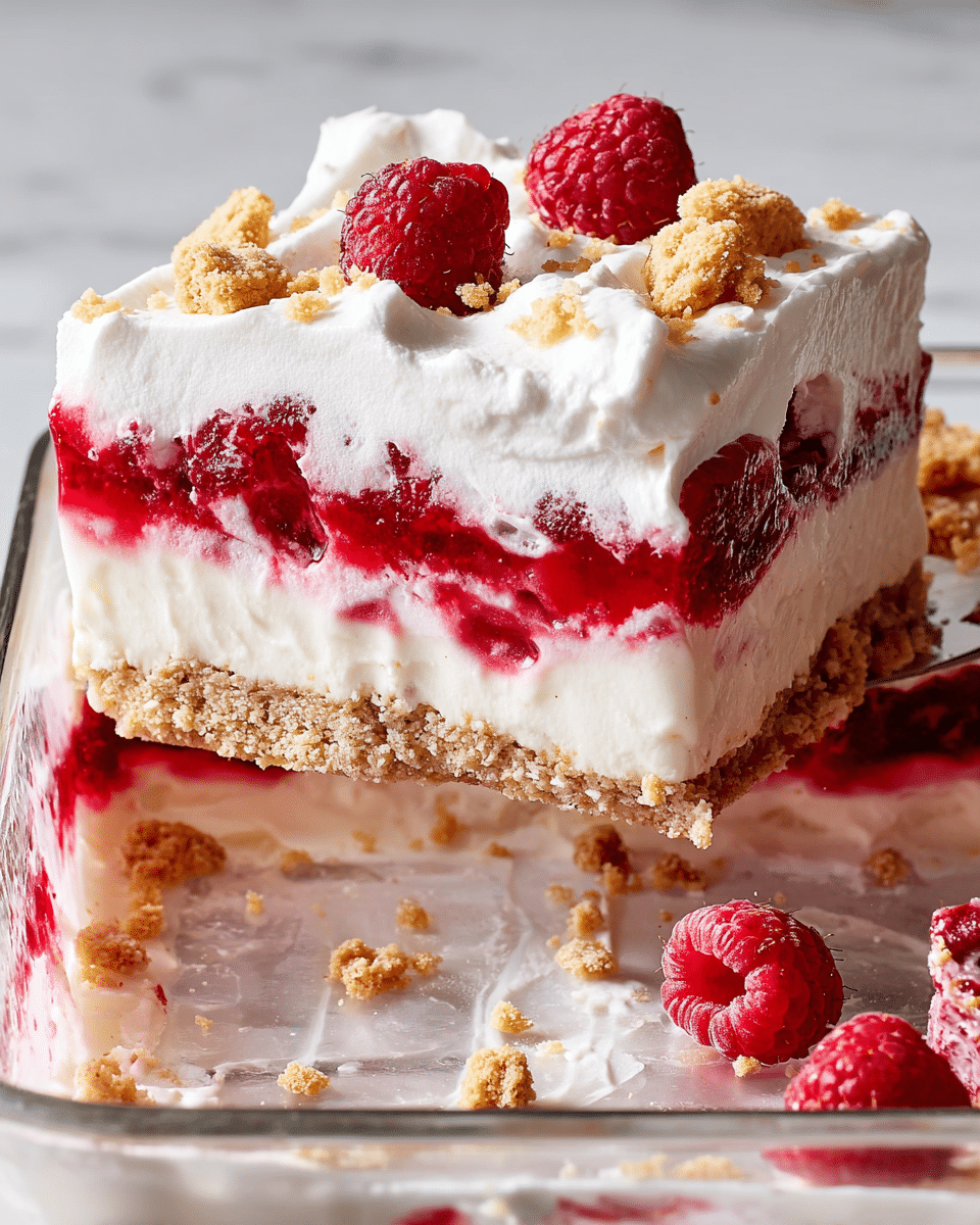 A square slice of raspberry dessert is lifted above a white marbled surface in a clear glass dish, showing four layers: a thick, crumbly light brown base, a smooth white creamy layer, a bright red raspberry jelly mixed with whole raspberries, and a thick white whipped cream topping. The whipped cream has some folds and small peaks with a few whole raspberries and small crumbled biscuit pieces scattered on top and around the dish. The clear glass dish reveals the red jelly layer pressed against the sides. photo taken with an iphone --ar 4:5 --v 7