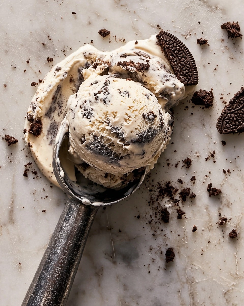 A scoop of creamy cookies and cream ice cream lies on a white marbled surface, showing its pale vanilla base mixed with dark chocolate cookie chunks. The ice cream scoop is melting slightly with swirls of cream and bits of cookie scattered around it. Next to the ice cream, there is a dark metal ice cream scooper with leftover melted ice cream inside the scoop part, resting on the surface. Small crumbs and pieces of cookie are spread around, adding texture to the scene. photo taken with an iphone --ar 4:5 --v 7