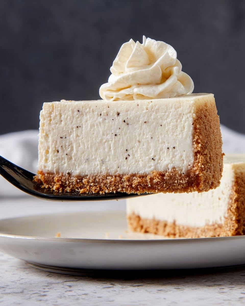 A slice of cream-colored cheesecake with two layers is being lifted by a utensil above a white plate, set against a white marbled textured background. The bottom layer is a crumbly, light brown crust that looks crunchy, while the top layer is thick, smooth, and creamy with tiny dark specks throughout, suggesting vanilla flavor. On top of the cheesecake slice, there is a small swirl of whipped cream adding softness and visual height. The image captures the dessert side on, showing clear separation between the crust and creamy filling. Photo taken with an iphone --ar 4:5 --v 7
