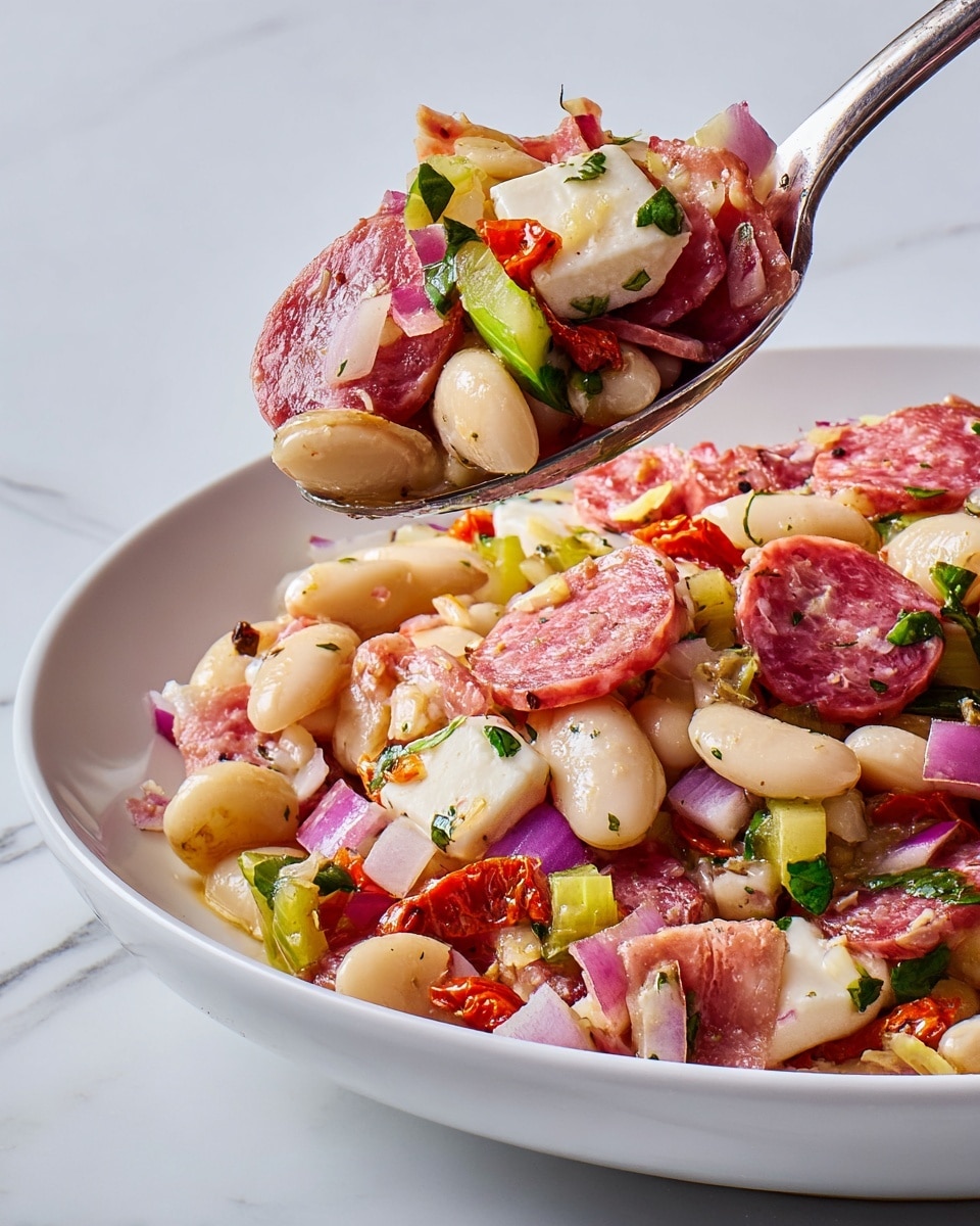 The image shows a close-up of a white plate filled with a colorful mixed salad. The bottom layer is made up of creamy white beans, visible throughout the dish. On top, there are many pieces of thinly sliced pinkish-red salami, scattered evenly. There are visible white chunks of mozzarella cheese, slightly browned and soft in texture. Mixed among these are small cubes of bright purple-red onion and pieces of green herbs, likely basil, scattered across the dish. There are also bits of red sun-dried tomatoes and light green celery slices, adding more color and texture. A silver spoon holds a generous scoop of the salad above the plate, showing all these ingredients mixed together with a light coating of oil and herbs. The background is a white marbled texture. Photo taken with an iphone --ar 4:5 --v 7