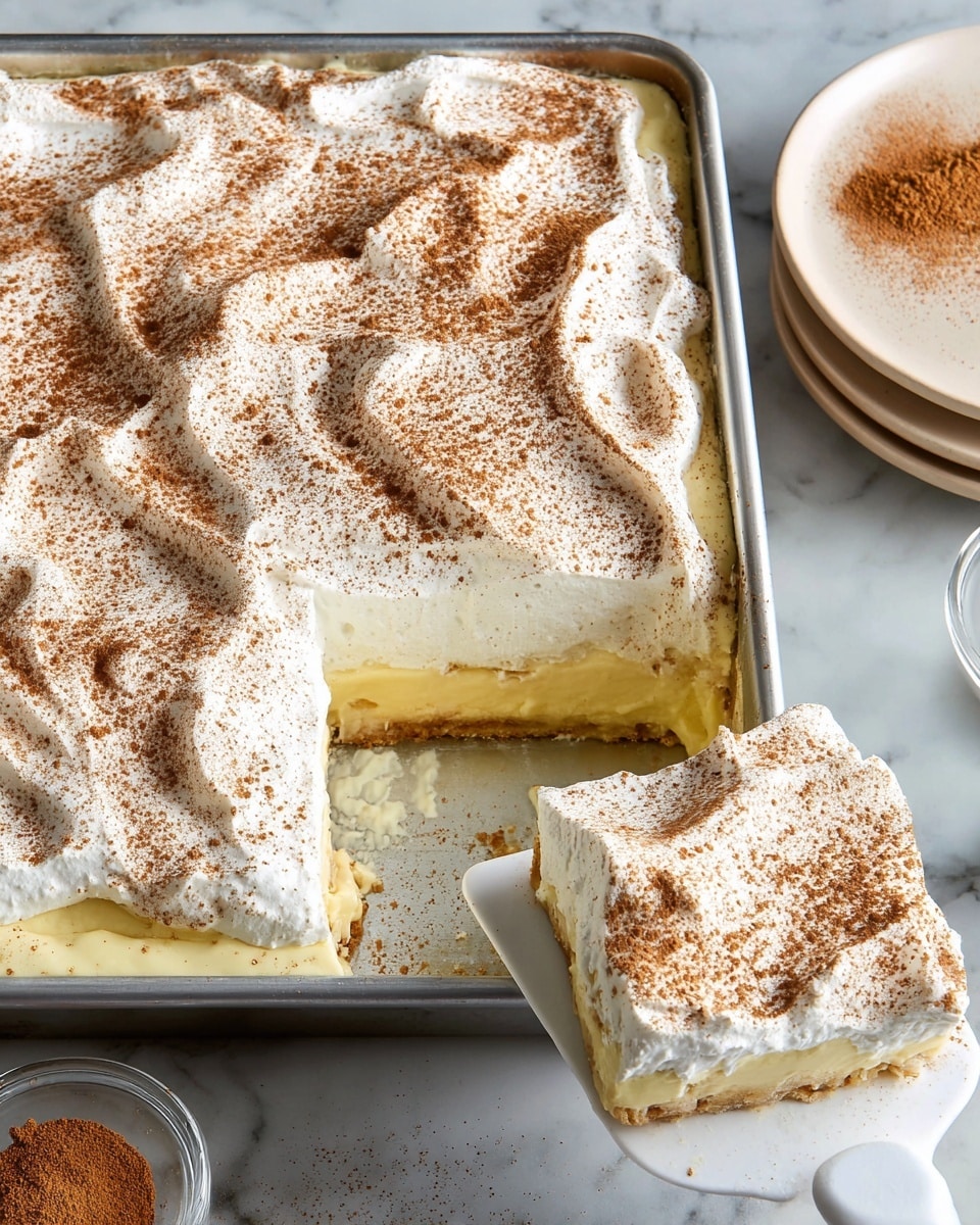 A rectangular metal baking pan filled with a creamy dessert shows three visible layers: the bottom layer is a light yellow custard with a smooth texture, the middle layer is not visible but implied, and the top layer is a thick, fluffy, white whipped topping dusted evenly with a light brown cinnamon powder, which creates a speckled pattern. A square piece of the dessert is lifted out with a white spatula, showing the creamy bottom layer underneath the whipped cream. The scene includes a white marbled surface beneath the pan and plates stacked beside it with a small glass bowl of cinnamon powder visible in the background. Photo taken with an iphone --ar 4:5 --v 7