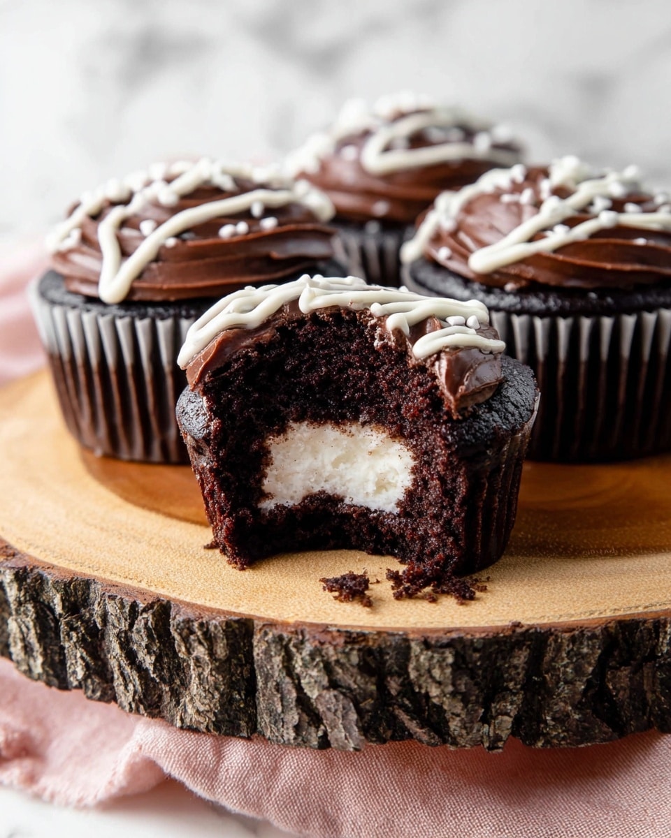 The image shows a group of four chocolate cupcakes on a natural wood stand with bark edges. The cupcake in front has a bite taken out, revealing three layers: a dark, moist chocolate cake base, a creamy white filling in the center, and a smooth dark chocolate frosting layer on top. Each cupcake is decorated with a drizzle of white icing on top, creating a slight swirl effect. The background is a white marbled texture, and a soft pink cloth is visible under the stand. photo taken with an iphone --ar 4:5 --v 7